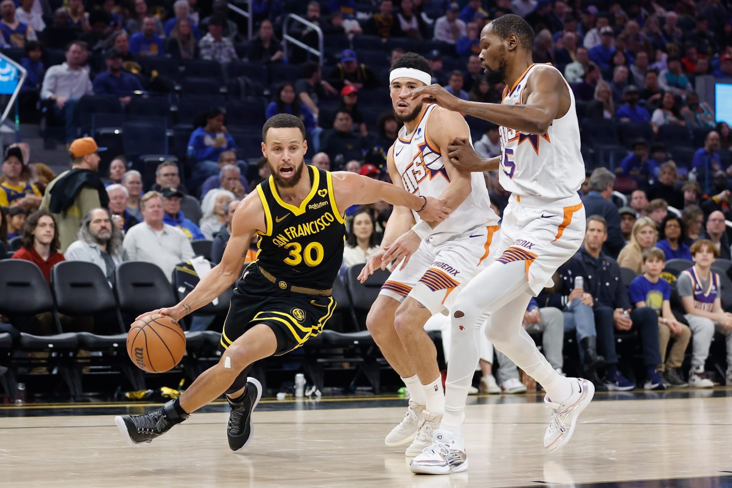 SAN FRANCISCO, CALIFORNIA - FEBRUARY 10: Stephen Curry #30 of the Golden State Warriors drives to the basket against Devin Booker #1 and Kevin Durant #35 of the Phoenix Suns in the third quarter at Chase Center on February 10, 2024 in San Francisco, California. NOTE TO USER: User expressly acknowledges and agrees that, by downloading and or using this photograph, User is consenting to the terms and conditions of the Getty Images License Agreement. (Photo by Lachlan Cunningham/Getty Images)
