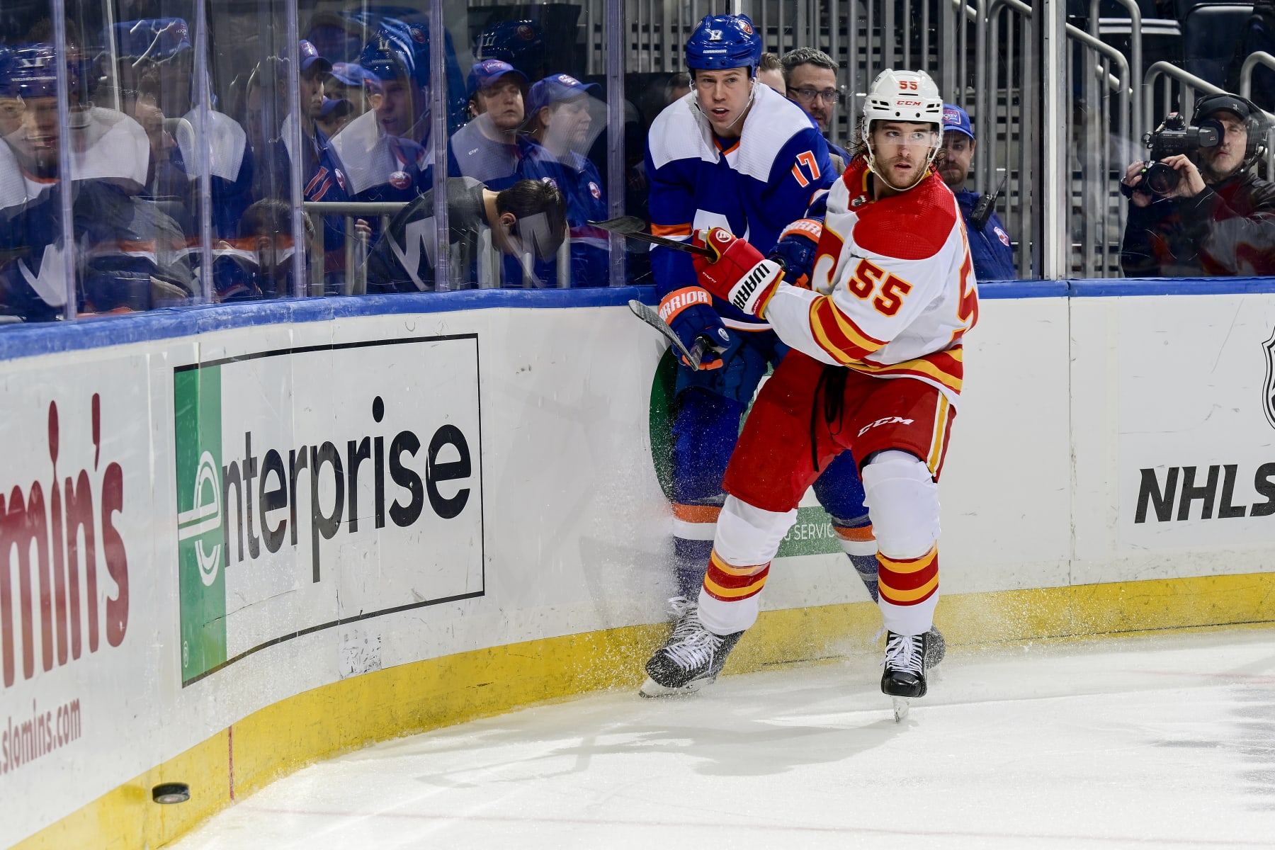ELMONT, NEW YORK - FEBRUARY 10:  Matt Martin #17 of the New York Islanders and Noah Hanifin #55 of the Calgary Flames pursue the puck during the third period at UBS Arena on February 10, 2024 in Elmont, New York. (Photo by Steven Ryan/NHLI via Getty Images)