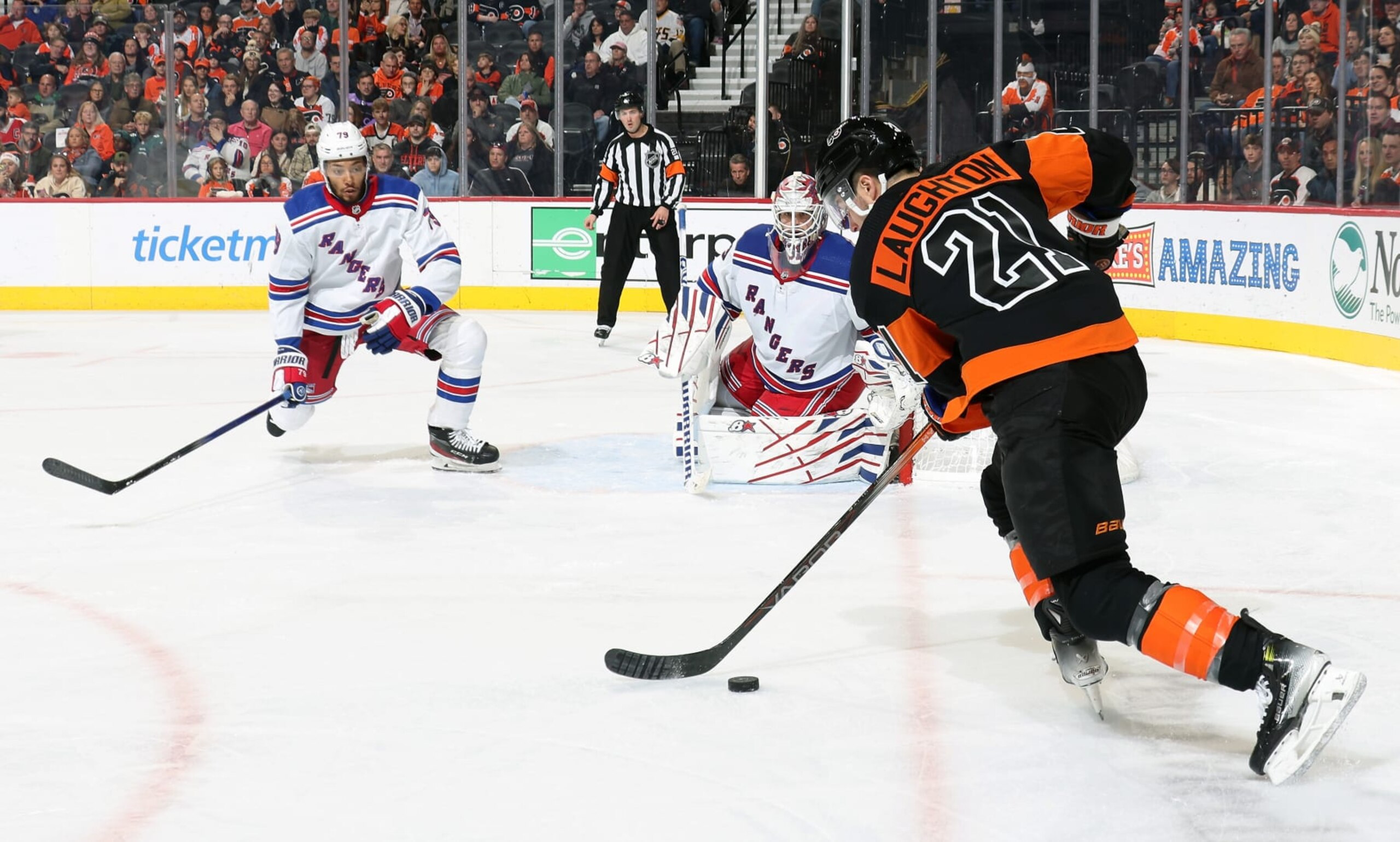 PHILADELPHIA, PENNSYLVANIA - NOVEMBER 24:  Scott Laughton #21 of the Philadelphia Flyers skates the puck along the goal line against K Andre Miller #79 and Igor Shesterkin #31 of the New York Rangers at the Wells Fargo Center on November 24, 2023 in Philadelphia, Pennsylvania.  (Photo by Len Redkoles/NHLI via Getty Images)