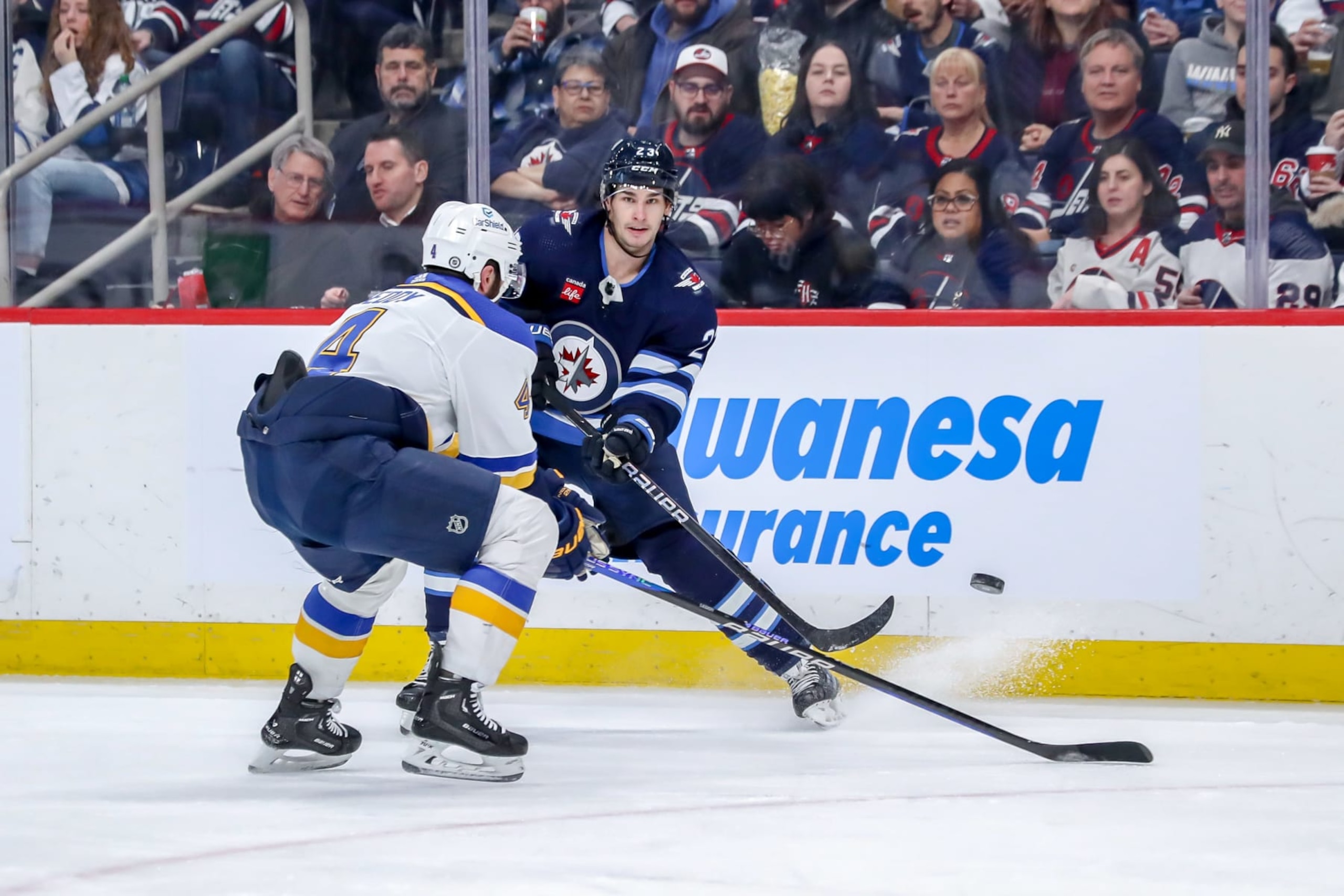 WINNIPEG, CANADA - FEBRUARY 27: Sean Monahan #23 of the Winnipeg Jets passes the puck over the stick of Nick Leddy #4 of the St. Louis Blues during second period action at the Canada Life Centre on February 27, 2024 in Winnipeg, Manitoba, Canada. (Photo by Darcy Finley/NHLI via Getty Images)