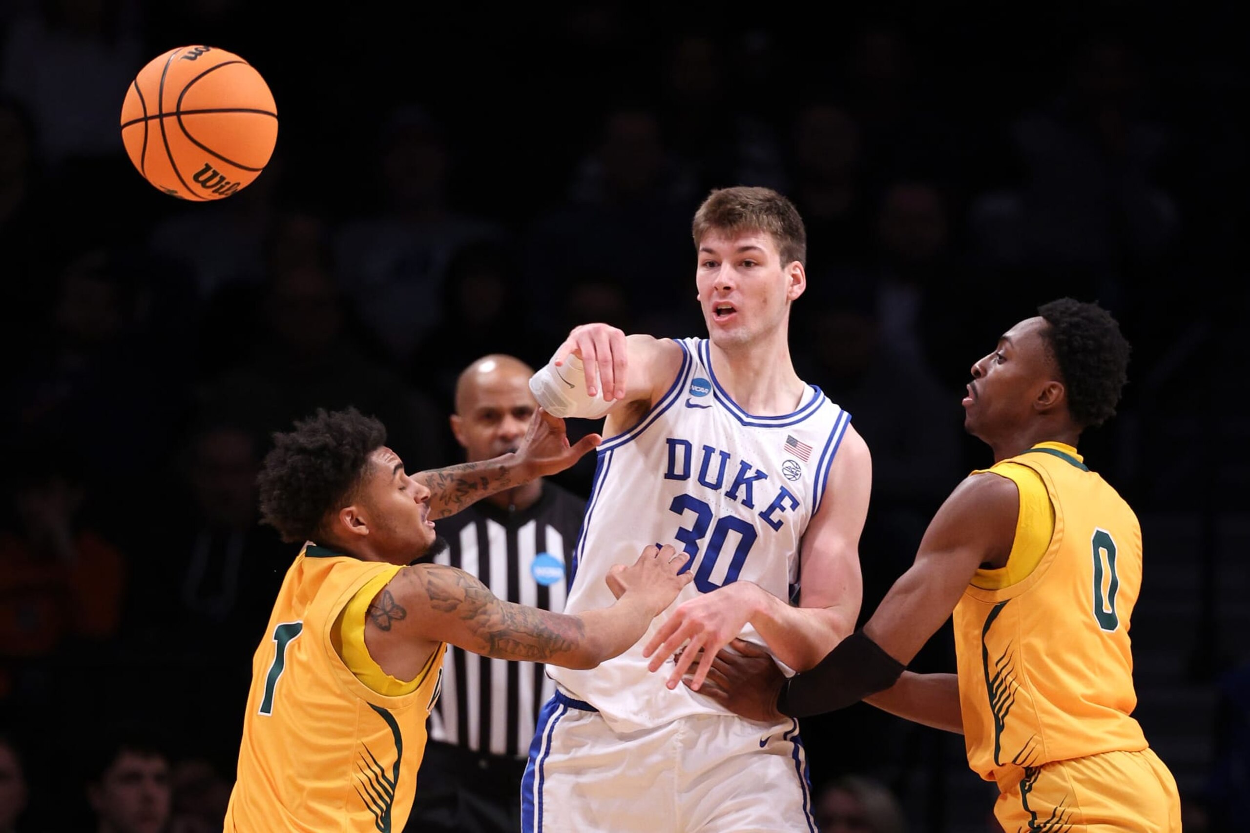 NEW YORK, NEW YORK - MARCH 22: Kyle Filipowski #30 of the Duke Blue Devils passes the ball between Aaron Deloney #1 and Ileri Ayo-Faleye #0 of the Vermont Catamounts during the first half in the first round of the NCAA Men's Basketball Tournament at Barclays Center on March 22, 2024 in New York City. (Photo by Elsa/Getty Images) NEW YORK, NEW YORK - MARCH 22: Kyle Filipowski #30 of the Duke Blue Devils passes the ball between Aaron Deloney #1 and Ileri Ayo-Faleye #0 of the Vermont Catamounts during the first half in the first round of the NCAA Men's Basketball Tournament at Barclays Center on March 22, 2024 in New York City. (Photo by Elsa/Getty Images)