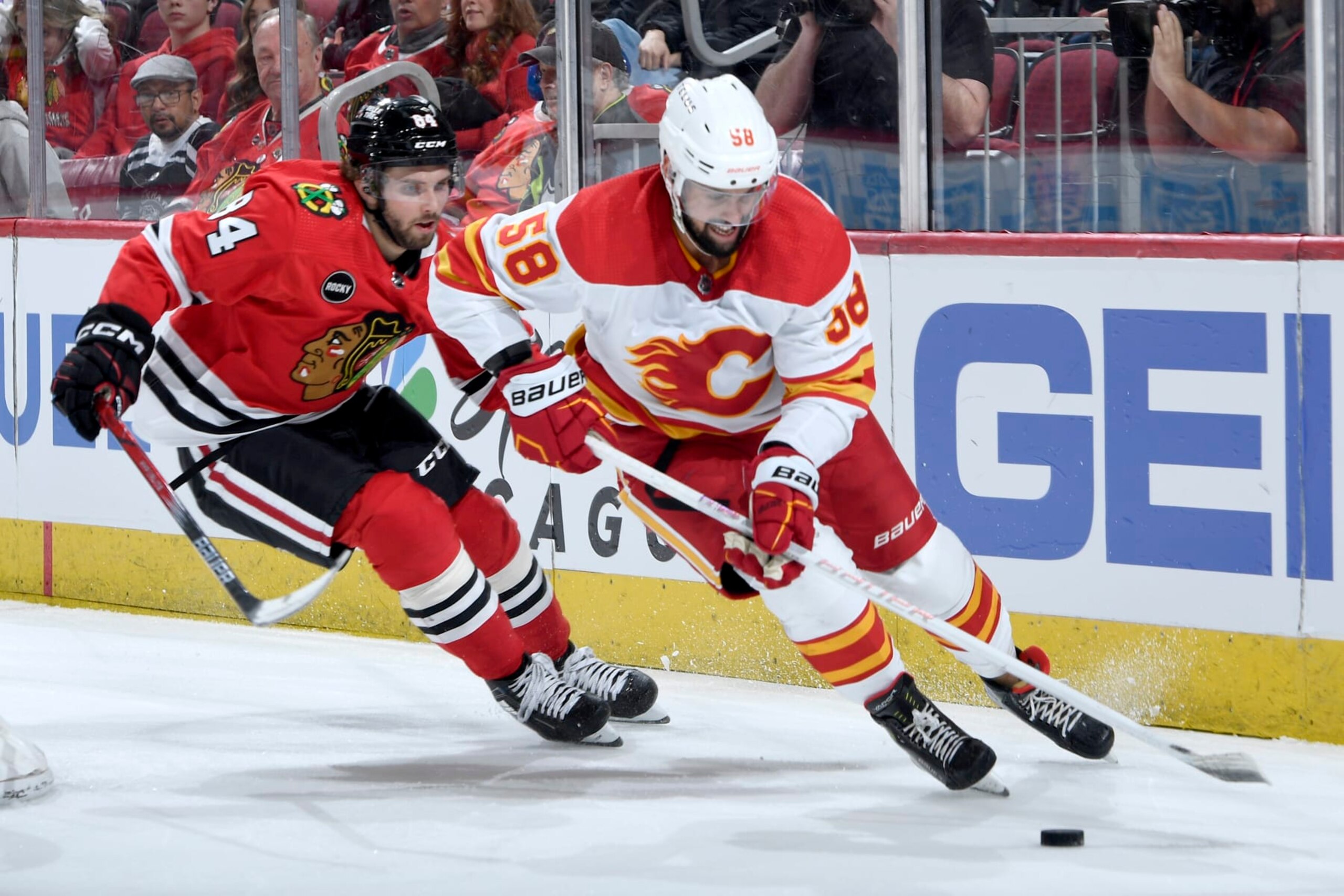 CHICAGO, ILLINOIS - MARCH 26: Oliver Kylington #58 of the Calgary Flames approaches the puck ahead of Landon Slaggert #84 of the Chicago Blackhawks in the third period at the United Center on March 26, 2024 in Chicago, Illinois. (Photo by Bill Smith/NHLI via Getty Images)