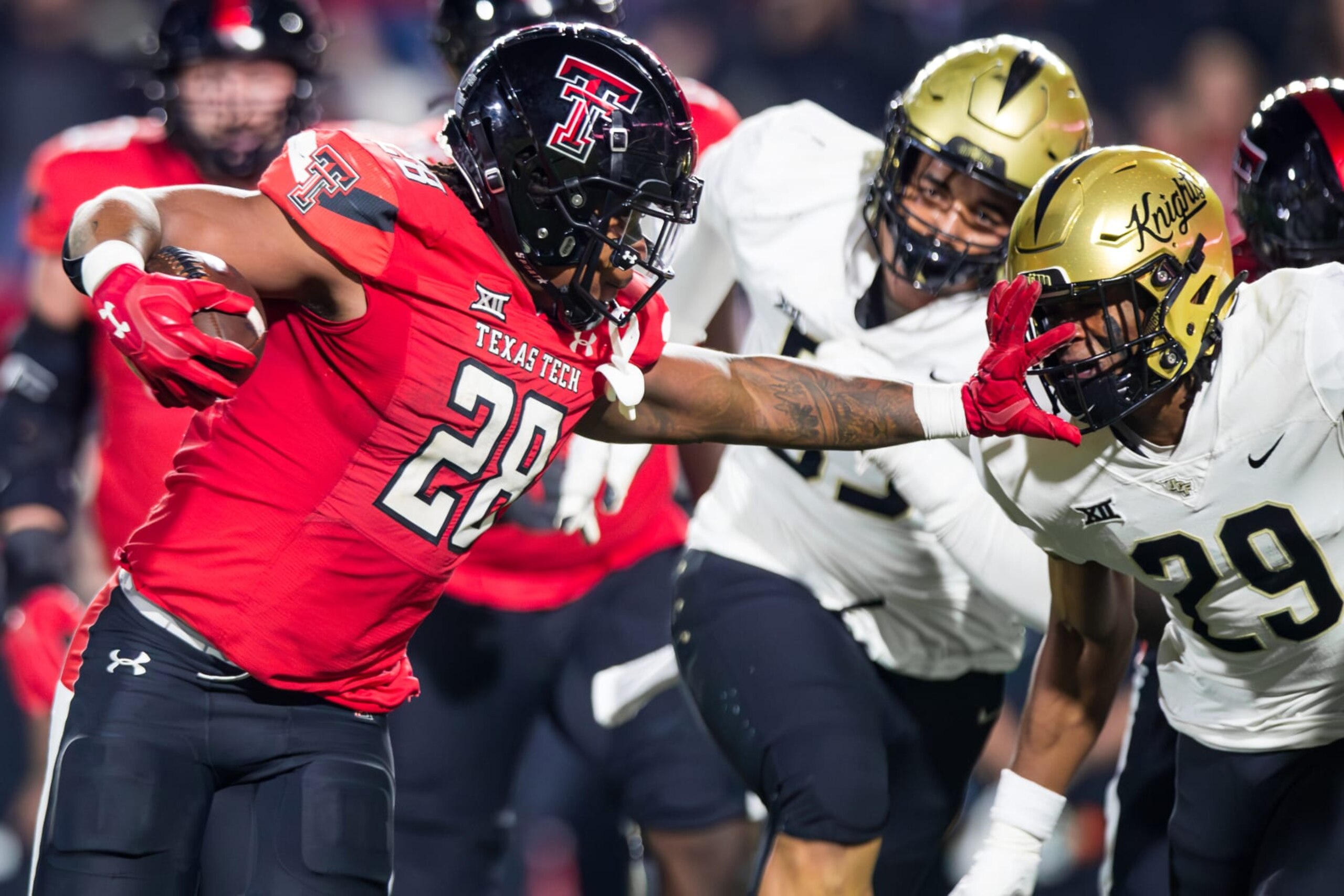 LUBBOCK, TEXAS - NOVEMBER 18: Tahj Brooks #28 of the Texas Tech Red Raiders stiff-arms William Wells #29 of the UCF Knights during the second half of the game at Jones AT&T Stadium on November 18, 2023 in Lubbock, Texas. (Photo by John E. Moore III/Getty Images)
