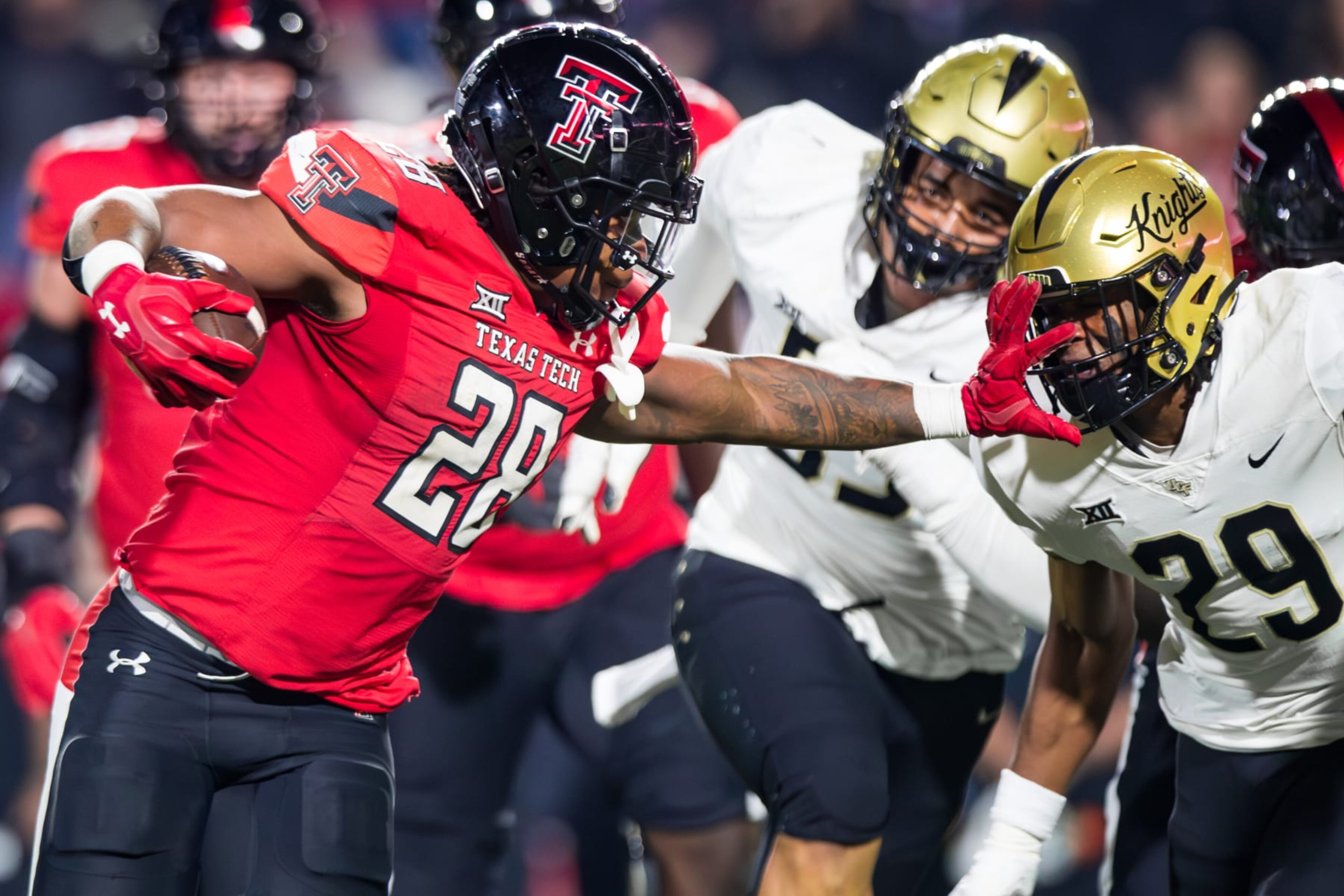 LUBBOCK, TEXAS - NOVEMBER 18: Tahj Brooks #28 of the Texas Tech Red Raiders stiff-arms William Wells #29 of the UCF Knights during the second half of the game at Jones AT&T Stadium on November 18, 2023 in Lubbock, Texas. (Photo by John E. Moore III/Getty Images)