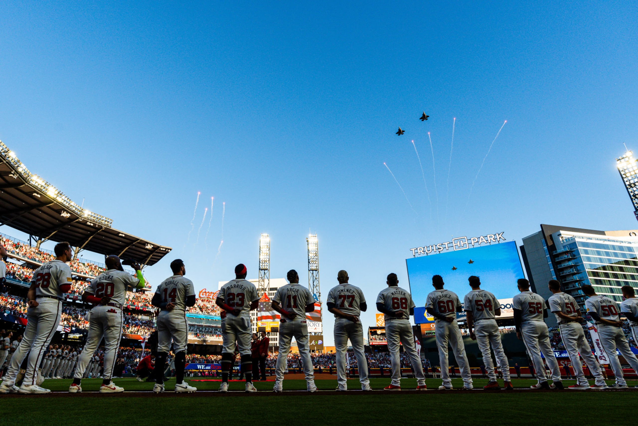 ATLANTA, GA - APRIL 05: Matt Olson #28, Marcell Ozuna #20, Adam Duvall #14, Michael Harris II #23, Orlando Arcia #11, Joe Jiménez #77, Tyler Matzek #68, Jesse Chavez #60, Max Fried #54, Dylan Lee #52, Chris Sale #51, and Charlie Morton #50 of the Atlanta Braves stand on the line during the national anthem flyover before the game against the Arizona Diamondbacks at Truist Park on Friday, April 5, 2024 in Atlanta, Georgia. (Matthew Grimes Jr./Atlanta Braves/Getty Images)
