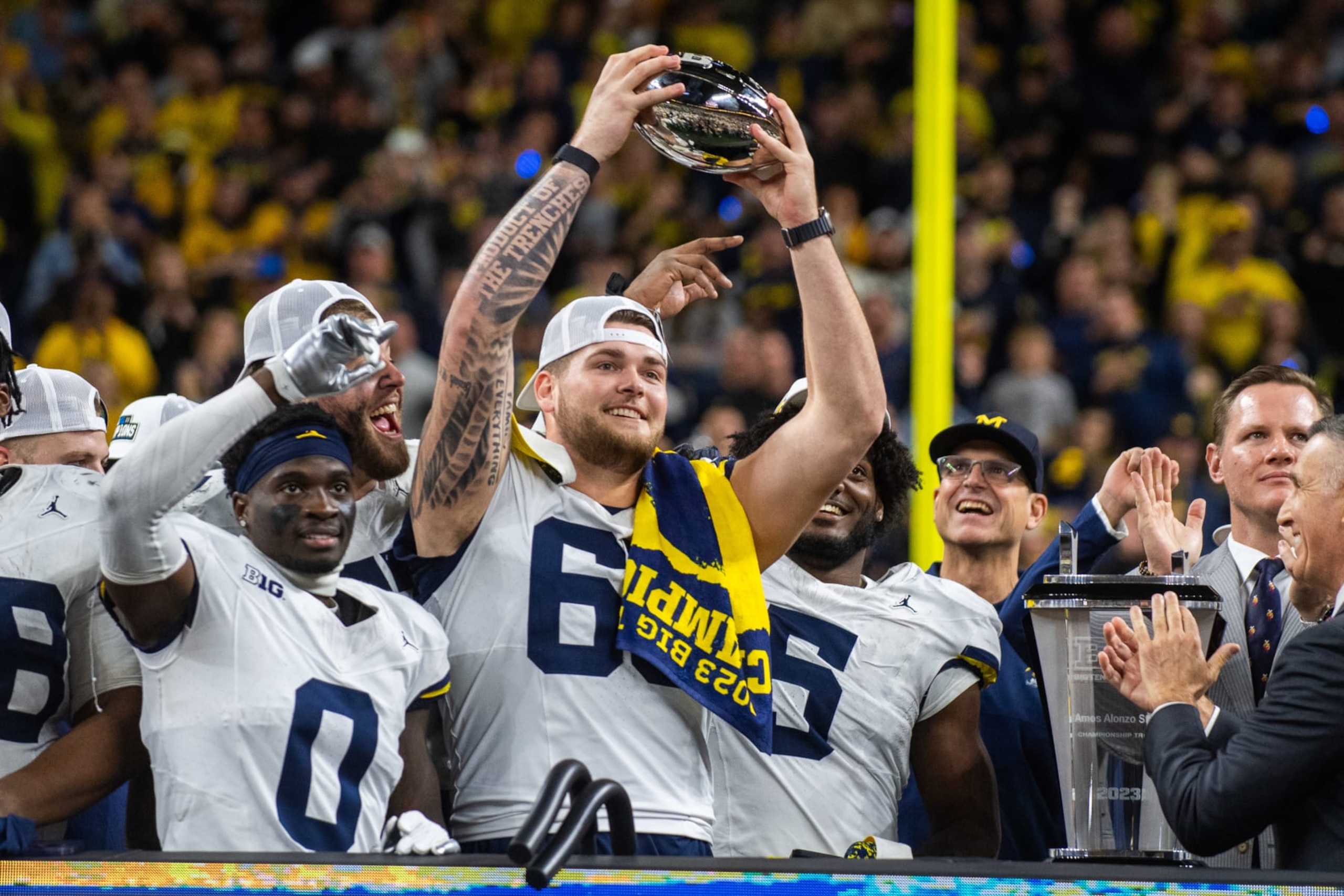 INDIANAPOLIS, INDIANA - DECEMBER 02:  (L-R) Mike Sainristil #0, Trevor Keegan #77, Zak Zinter #65, and Josaiah Stewart #5 of the Michigan Wolverines celebrate with the Big Ten Championship trophy after winning the Big Ten Championship against the Iowa Hawkeyes at Lucas Oil Stadium on December 02, 2023 in Indianapolis, Indiana. The Michigan Wolverines won the game 26-0. (Photo by Aaron J. Thornton/Getty Images)