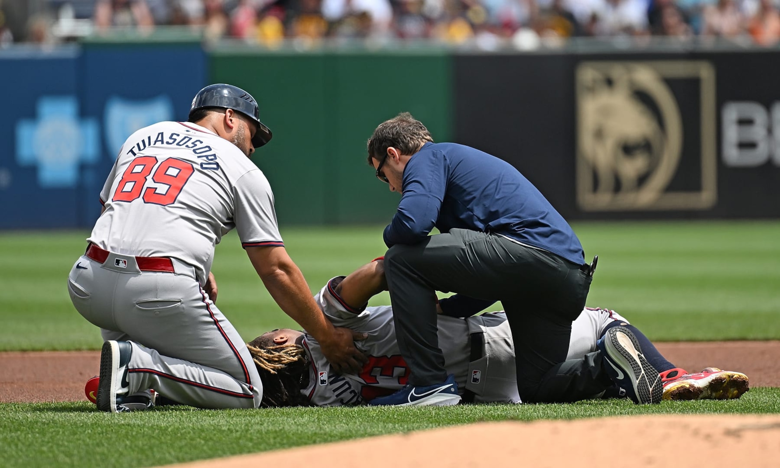 PITTSBURGH, PENNSYLVANIA - MAY 26: Ronald Acuña Jr. #13 of the Atlanta Braves is attended to by a trainer and third base coach Matt Tuiasosopo #89 after falling to the ground with an apparent injury in the first inning during the game against the Pittsburgh Pirates at PNC Park on May 26, 2024 in Pittsburgh, Pennsylvania. (Photo by Justin Berl/Getty Images)