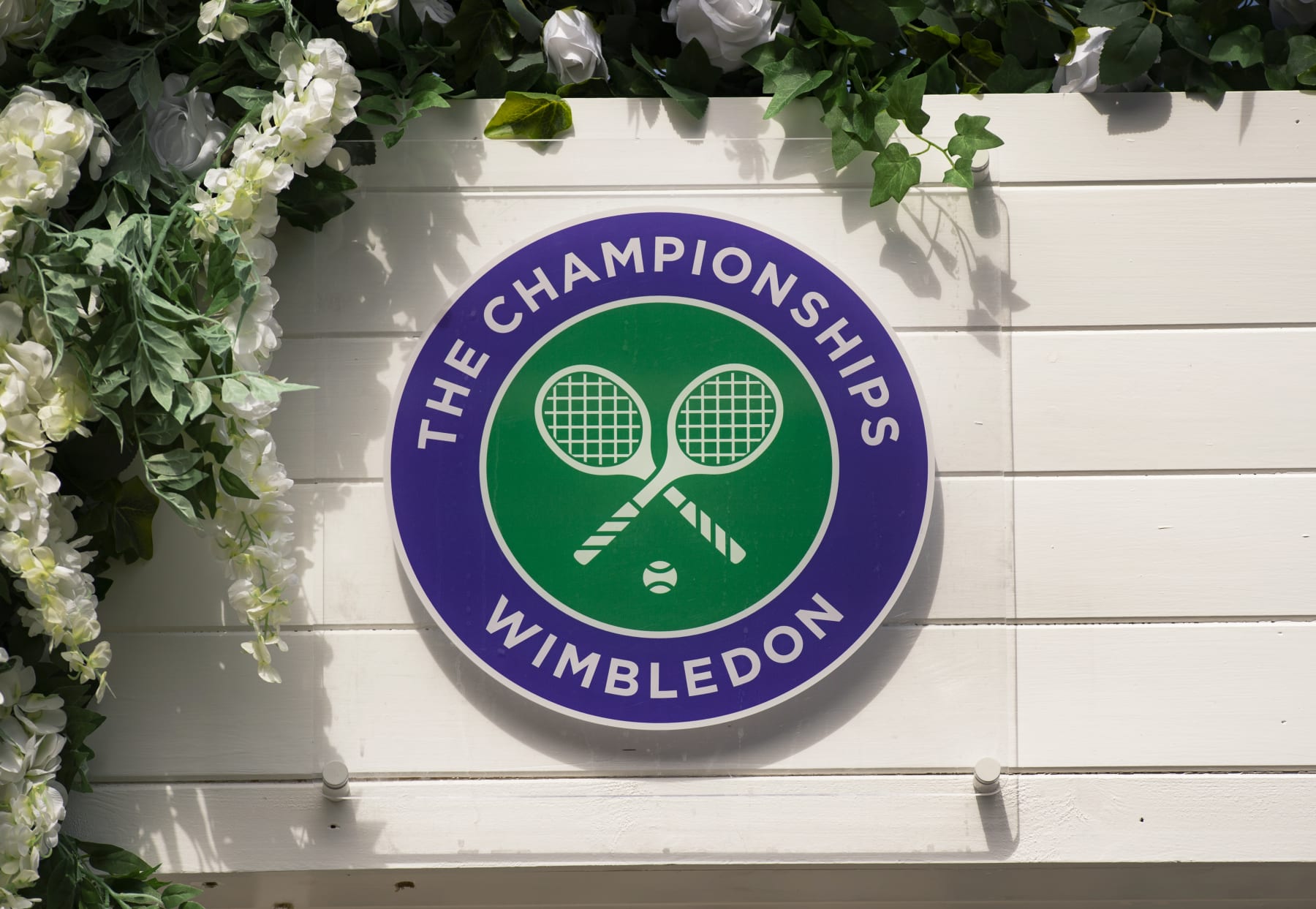 LONDON, ENGLAND - JULY 11: The Wimbledon logo surrounded by flowers during Day Ten of The Championships - Wimbledon 2019 at All England Lawn Tennis and Croquet Club on July 11, 2019 in London, England. (Photo by Visionhaus/Getty Images)