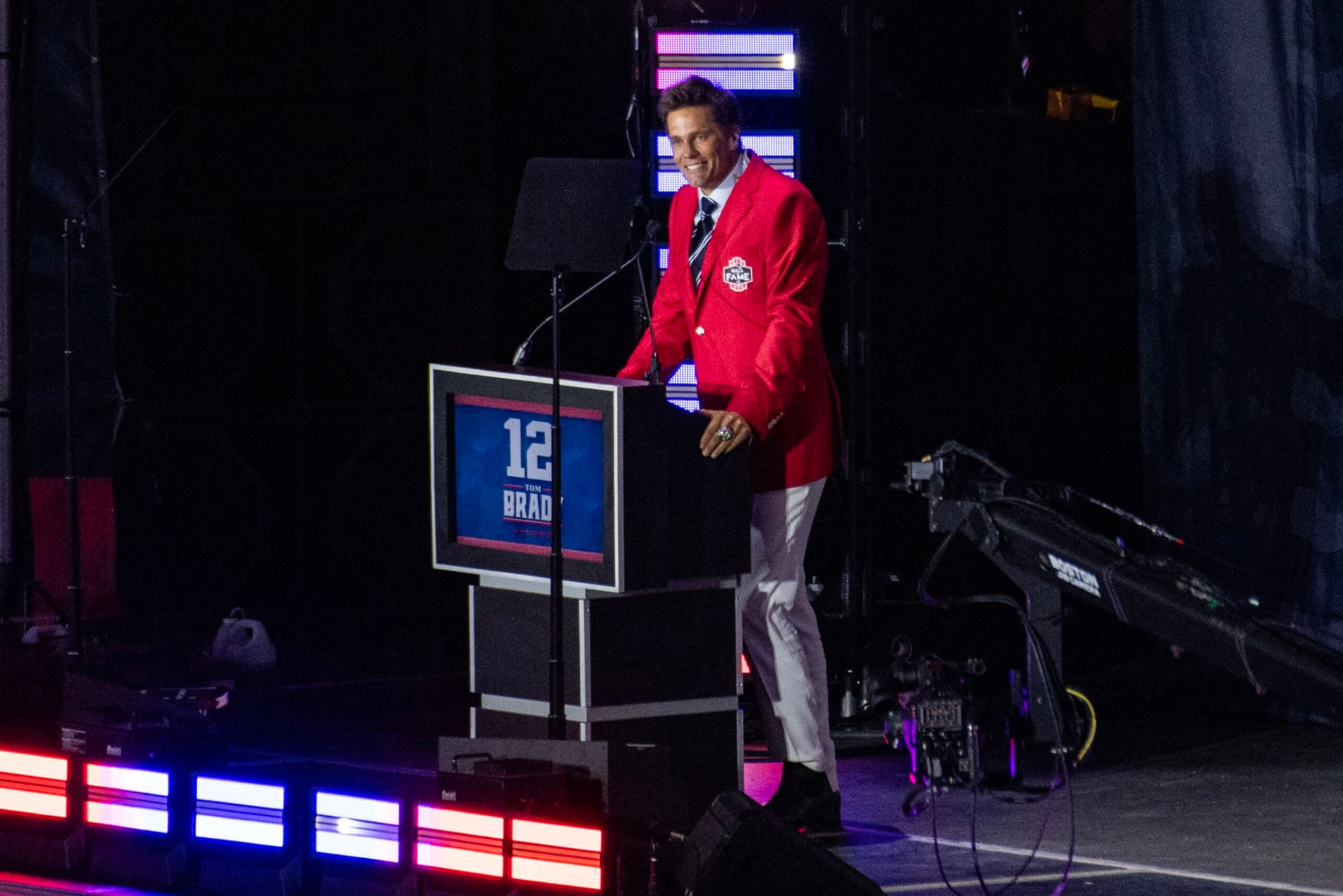 Former New England Patriots quarterback Tom Brady wears his red Patriots Hall of Fame induction jacket as he speaks during the 2024 induction ceremony at Gillette Stadium in Foxborough, Massachusetts, on June 12, 2024. Tom Brady is the 35th person to be inducted into the Patriots Hall of Fame. (Photo by Joseph Prezioso / AFP) (Photo by JOSEPH PREZIOSO/AFP via Getty Images)