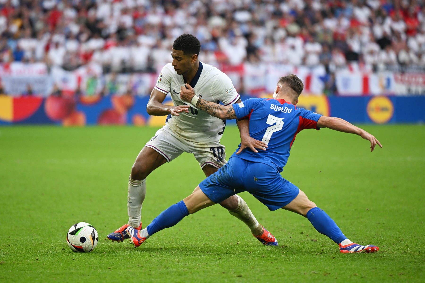GELSENKIRCHEN, GERMANY - JUNE 30: Jude Bellingham of England is challenged by Tomas Suslov of Slovakia during the UEFA EURO 2024 round of 16 match between England and Slovakia at Arena AufSchalke on June 30, 2024 in Gelsenkirchen, Germany. (Photo by Clive Mason/Getty Images)