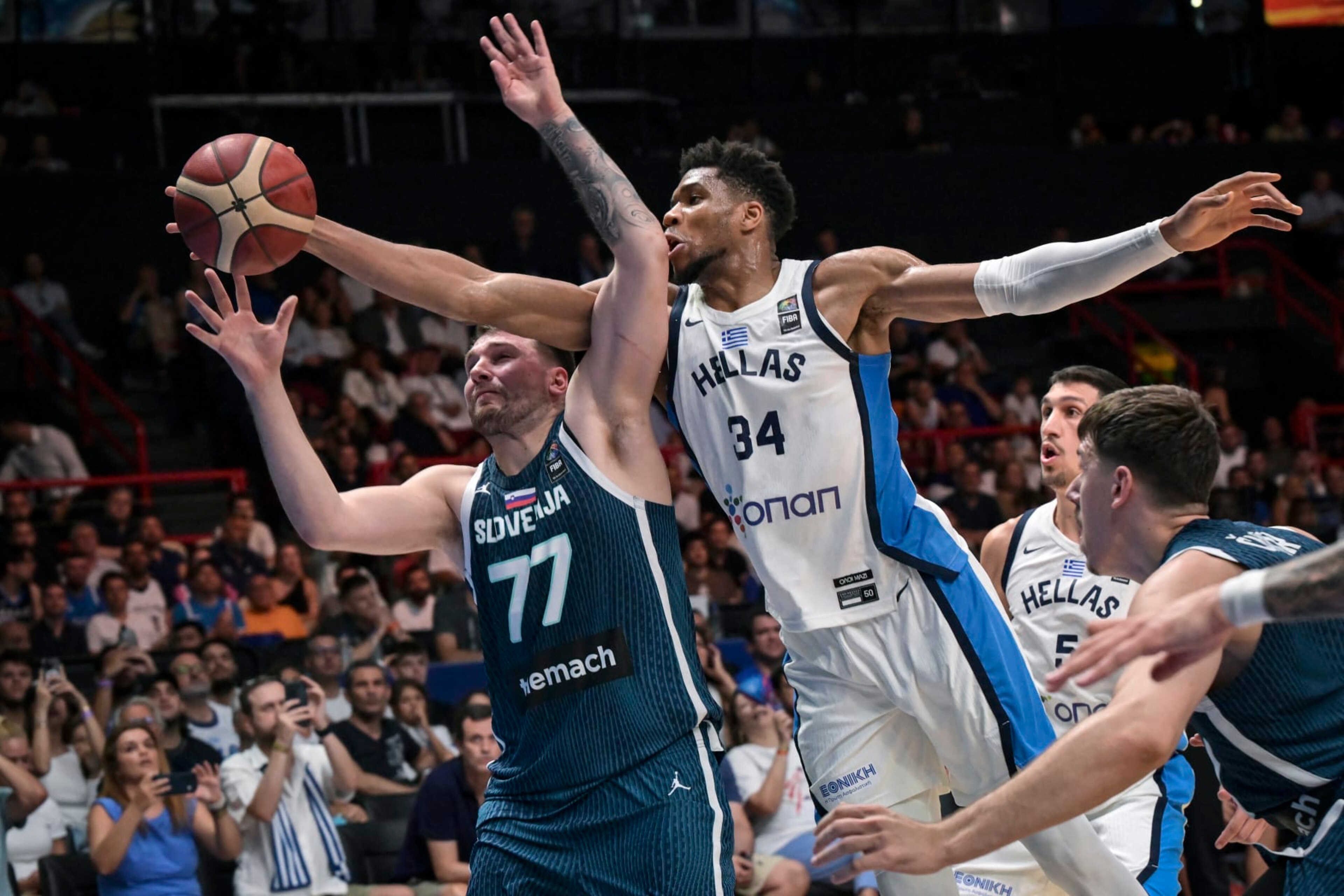 Greece's Giannis Antentokoumbo (C) jumps for a rebound with Slovenia's Luka Doncic (L) during the 2024 FIBA Olympic Qualifying Tournament semi-final basketball match between Dominican Republic and Greece at the Peace and Friendship Stadium in Athens, on July 6, 2024. (Photo by Aris MESSINIS / AFP) (Photo by ARIS MESSINIS/AFP via Getty Images)