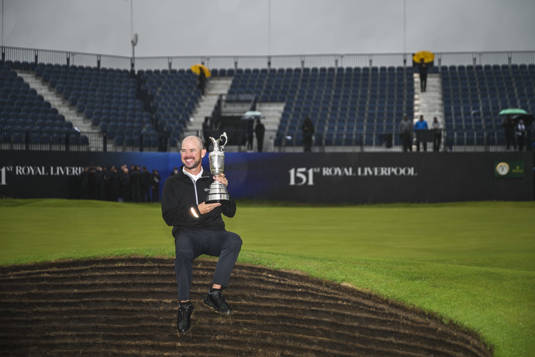 HOYLAKE, ENGLAND - JULY 23:  Brian Harman smiles with the Claret Jug trophy as he sits along a pot bunker following his six stroke victory in the final round of The 151st Open Championship at Royal Liverpool Golf Club on July 23, 2023 in Hoylake, England. (Photo by Keyur Khamar/PGA TOUR via Getty Images)