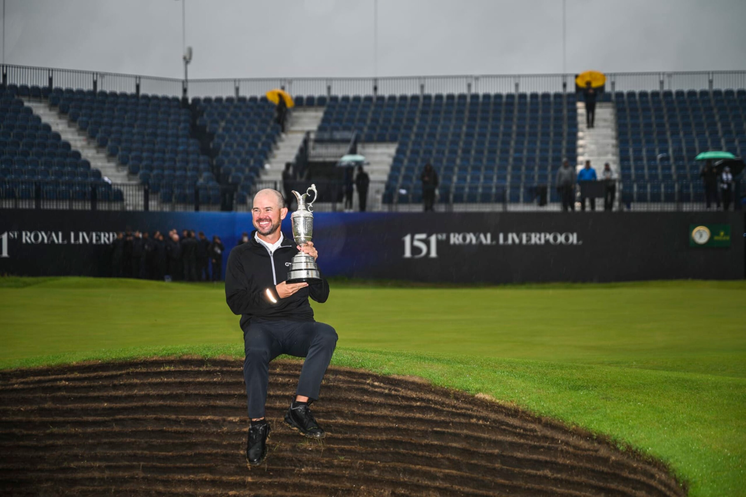 HOYLAKE, ENGLAND - JULY 23:  Brian Harman smiles with the Claret Jug trophy as he sits along a pot bunker following his six stroke victory in the final round of The 151st Open Championship at Royal Liverpool Golf Club on July 23, 2023 in Hoylake, England. (Photo by Keyur Khamar/PGA TOUR via Getty Images)