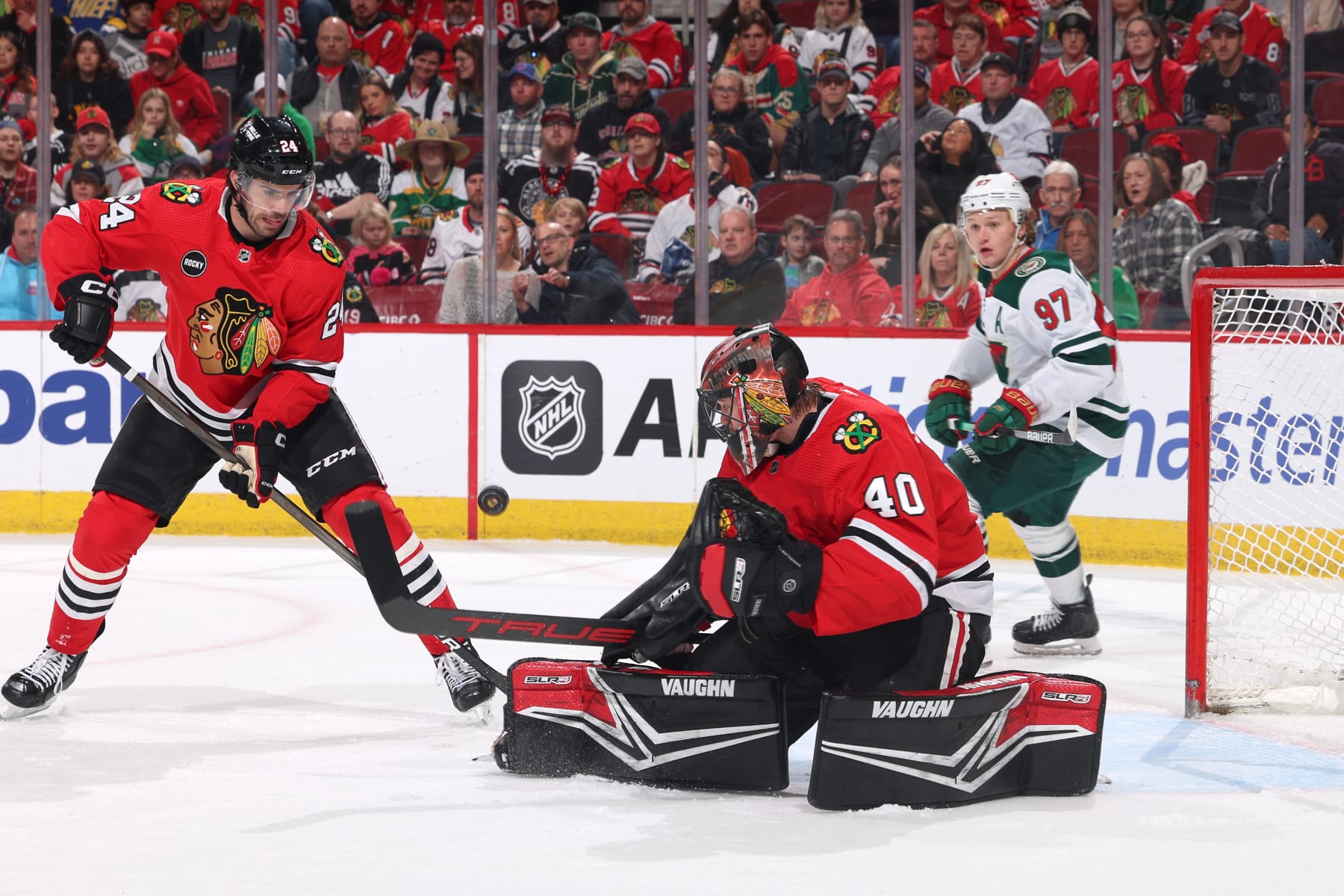 CHICAGO, ILLINOIS - APRIL 07: Jaycob Megna #24 and goalie Arvid Soderblom #40 of the Chicago Blackhawks watch the puck in the first period against the Minnesota Wild at the United Center on April 07, 2024 in Chicago, Illinois. (Photo by Chase Agnello-Dean/NHLI via Getty Images)