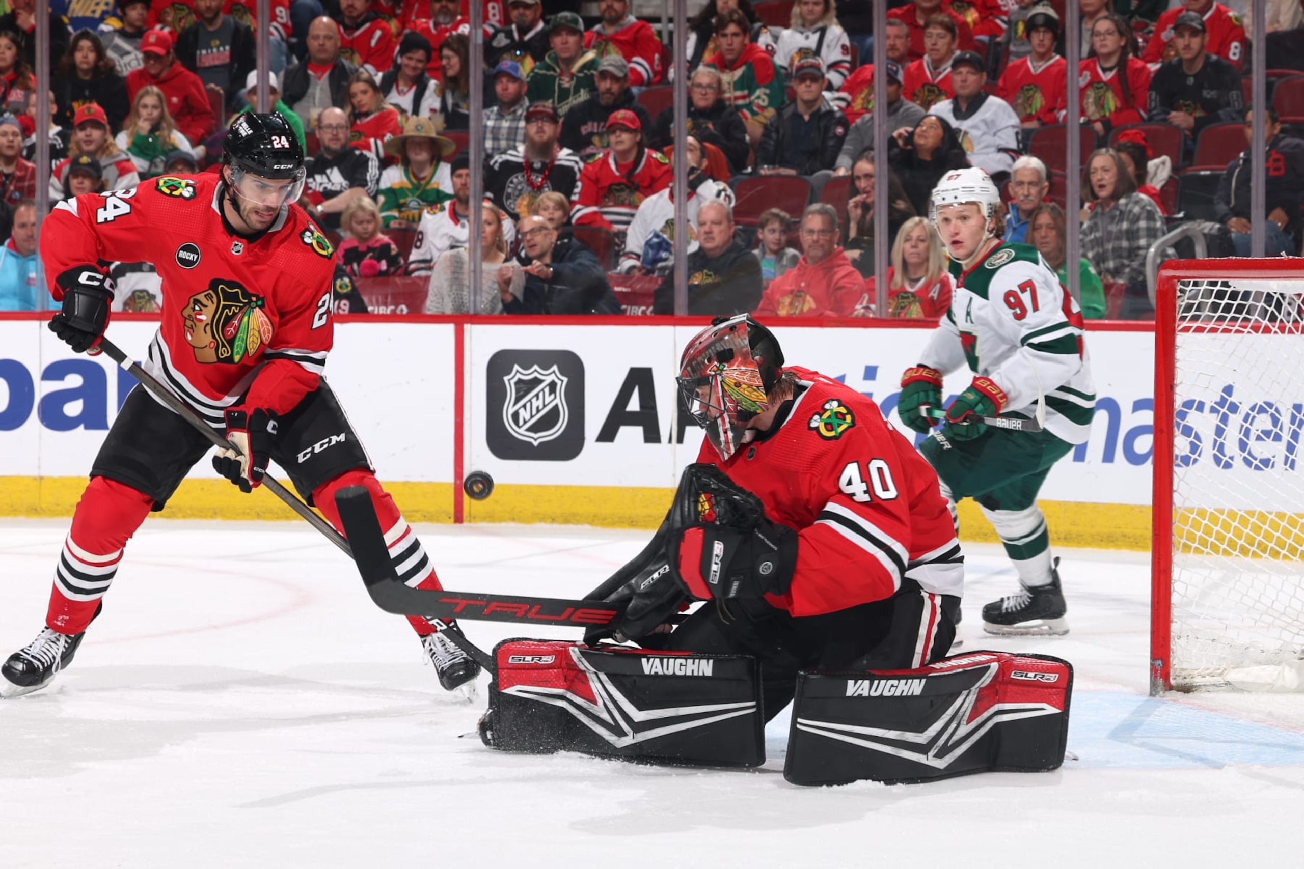 CHICAGO, ILLINOIS - APRIL 07: Jaycob Megna #24 and goalie Arvid Soderblom #40 of the Chicago Blackhawks watch the puck in the first period against the Minnesota Wild at the United Center on April 07, 2024 in Chicago, Illinois. (Photo by Chase Agnello-Dean/NHLI via Getty Images)