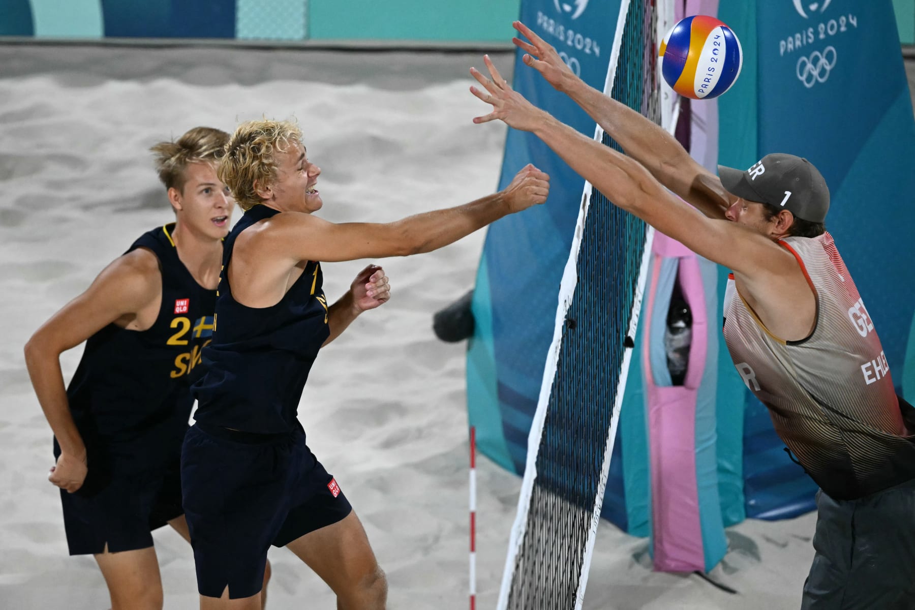 Sweden's #01 David Ahman spikes the ball beside his partner Sweden's #02 Jonatan Hellvig as Germany's #01 Nils Ehlers blocks in the men's gold medal beach volleyball match between Sweden and Germany during the Paris 2024 Olympic Games at the Eiffel Tower Stadium in Paris on August 10, 2024. (Photo by CARL DE SOUZA / AFP) (Photo by CARL DE SOUZA/AFP via Getty Images)