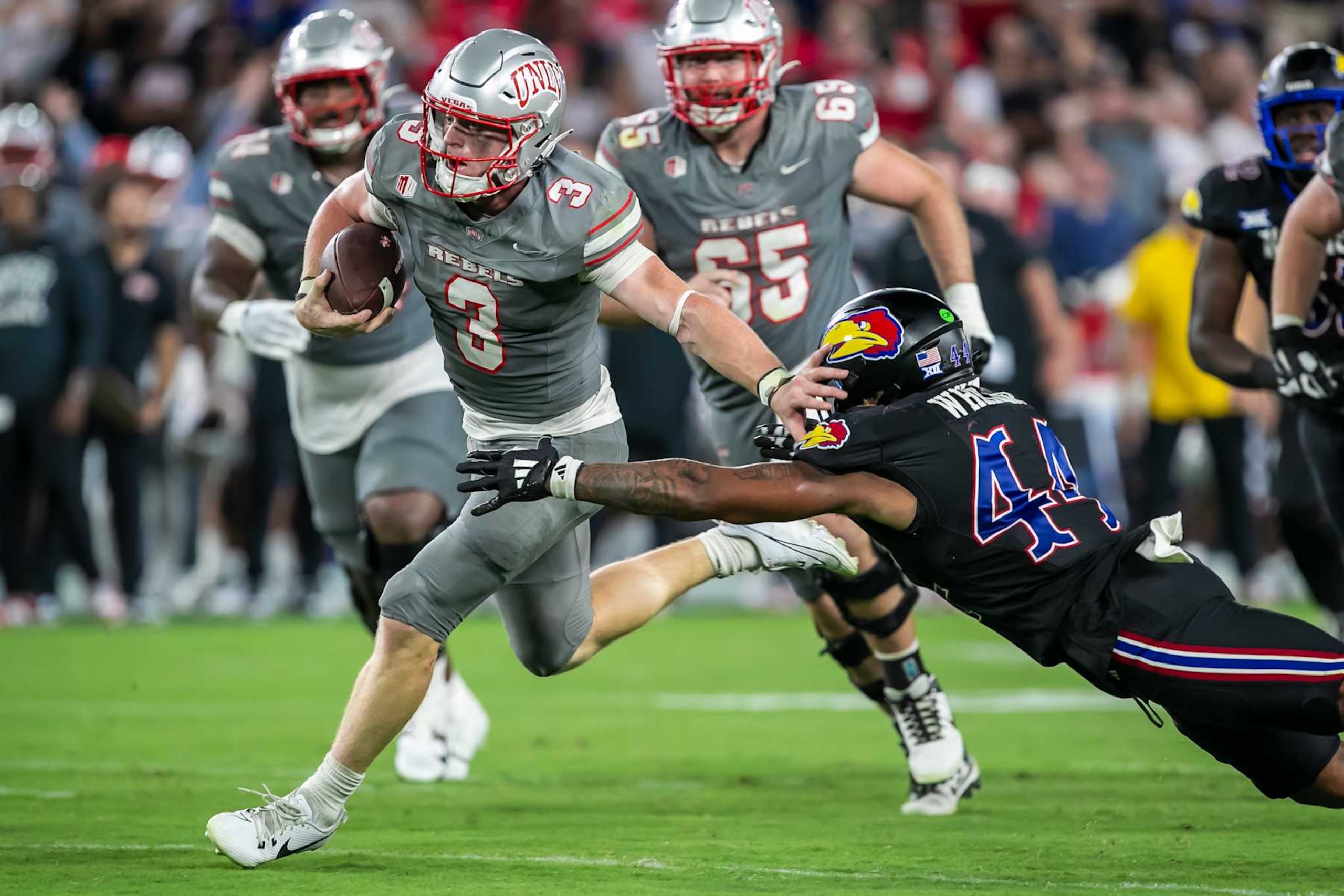 KANSAS CITY, KS - SEPTEMBER 13:UNLV quarterback Matthew Sluka (3) scrambles past the tackle of Kansas linebacker Cornell Wheeler (44) during the game between the Kansas Jayhawks and the UNLV Rebels on Friday September 13, 2024 at Children's Mercy Park in Kansas City, Kansas.  (Photo by Nick Tre. Smith/Icon Sportswire via Getty Images)