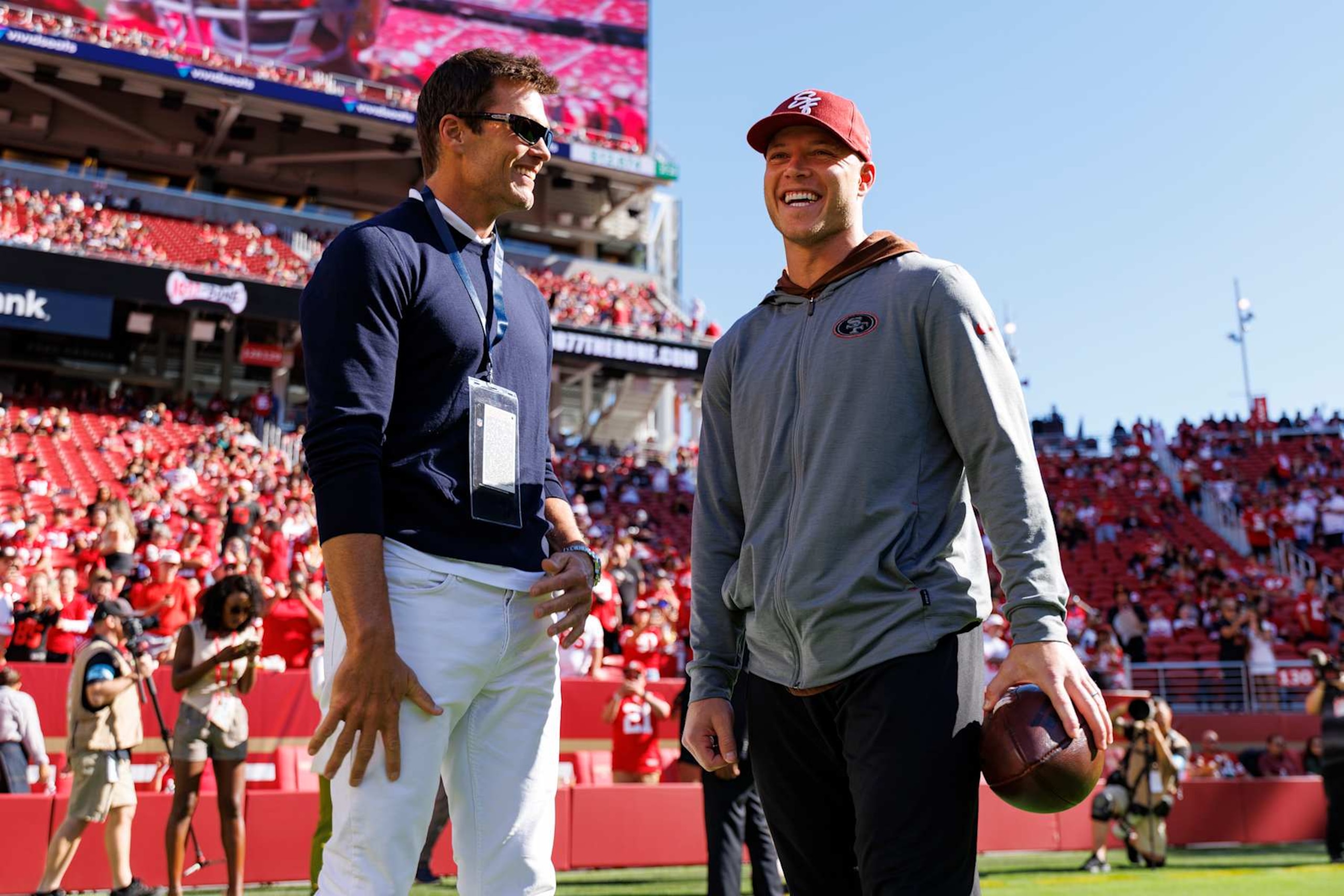 SANTA CLARA, CA - AUGUST 18: Fox on-air host and former NFL quarterback Tom Brady interacts with running back Christian McCaffrey #23 of the San Francisco 49ers prior to an NFL preseason football game between the New Orleans Saints and the San Francisco 49ers at Levi's Stadium on August 18, 2024 in Santa Clara, California. (Photo by Brooke Sutton/Getty Images)