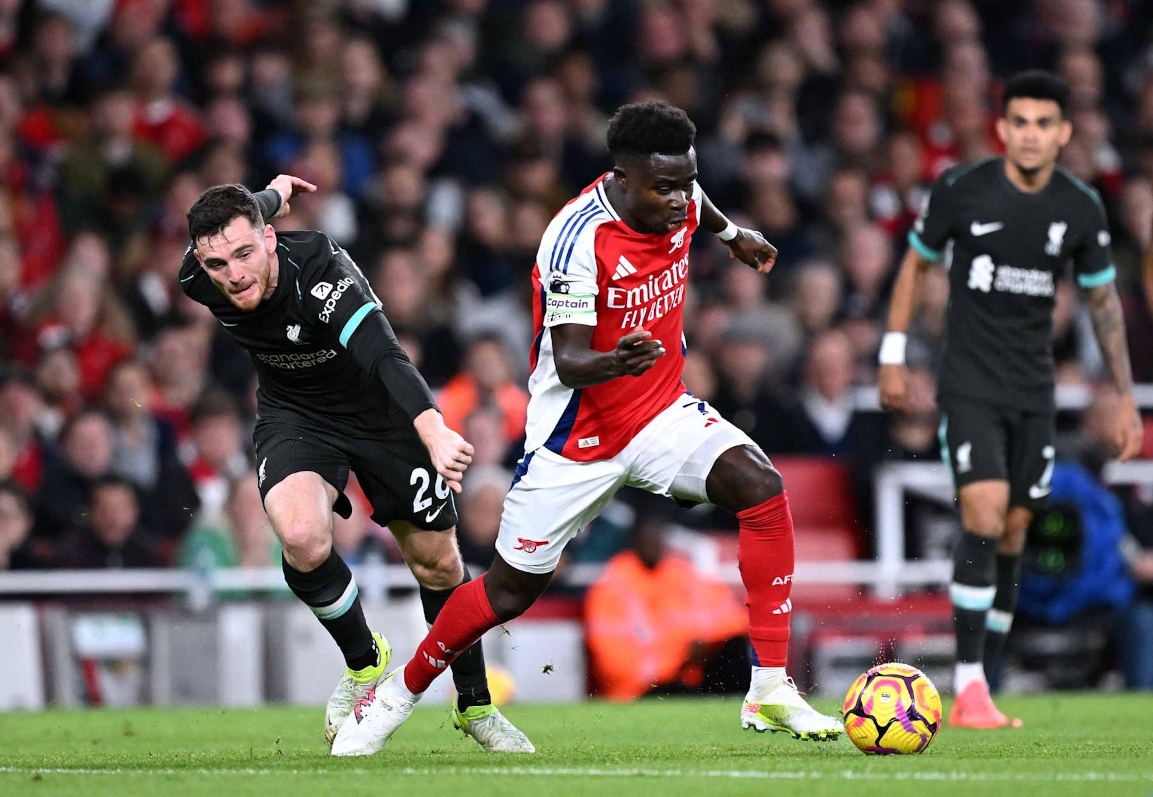 LONDON, ENGLAND - OCTOBER 27: Bukayo Saka of Arsenal runs with the ball whilst under pressure from Andrew Robertson of Liverpool during the Premier League match between Arsenal FC and Liverpool FC at Emirates Stadium on October 27, 2024 in London, England. (Photo by David Price/Arsenal FC via Getty Images)