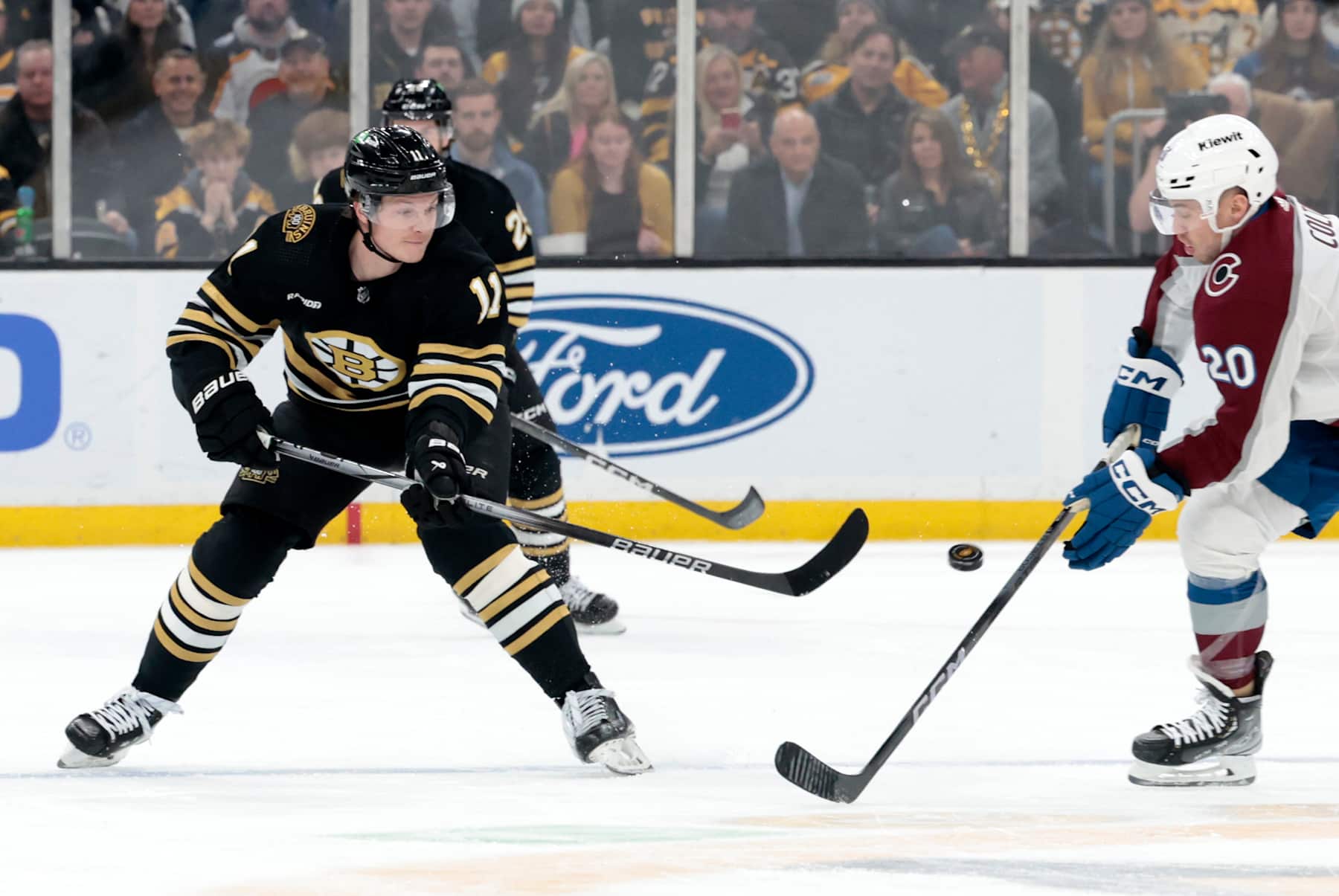 BOSTON, MA - JANUARY 18: Boston Bruins center Trent Frederic (11) shovels the puck past Colorado Avalanche center Ross Colton (20) during a game between the Boston Bruins and the Colorado Rapids on January 18, 2024, at TD Garden in Boston, Massachusetts. (Photo by Fred Kfoury III/Icon Sportswire via Getty Images)