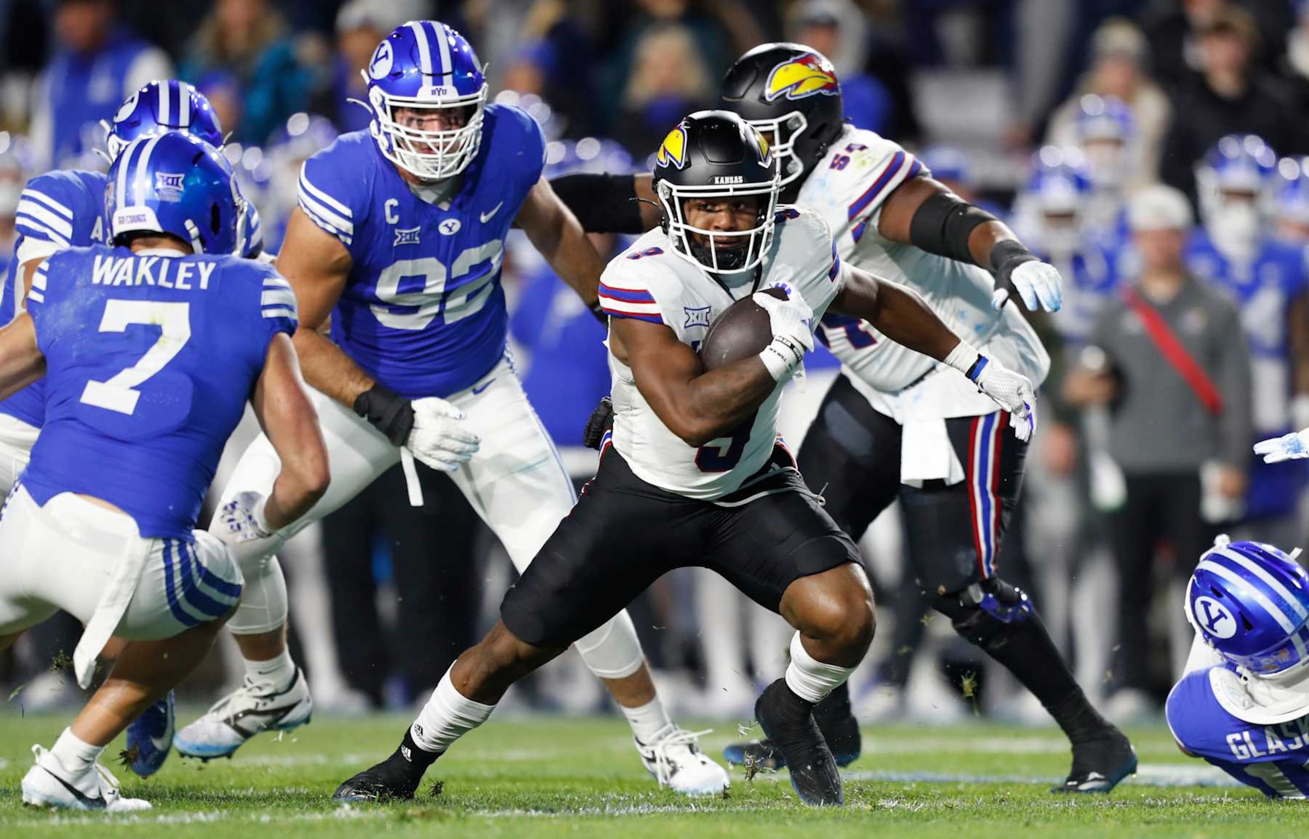 PROVO, UT - NOVEMBER 16:  Daniel Hishaw #9 of the Kansas Jayhawks rushes the ball against Crew Wakley #7 and Tyler Batty #92 of the Brigham Young Cougars during the first half of their game at LaVell Edwards Stadium on November 16, 2024 in Provo, Utah.(Photo by Chris Gardner/Getty Images)