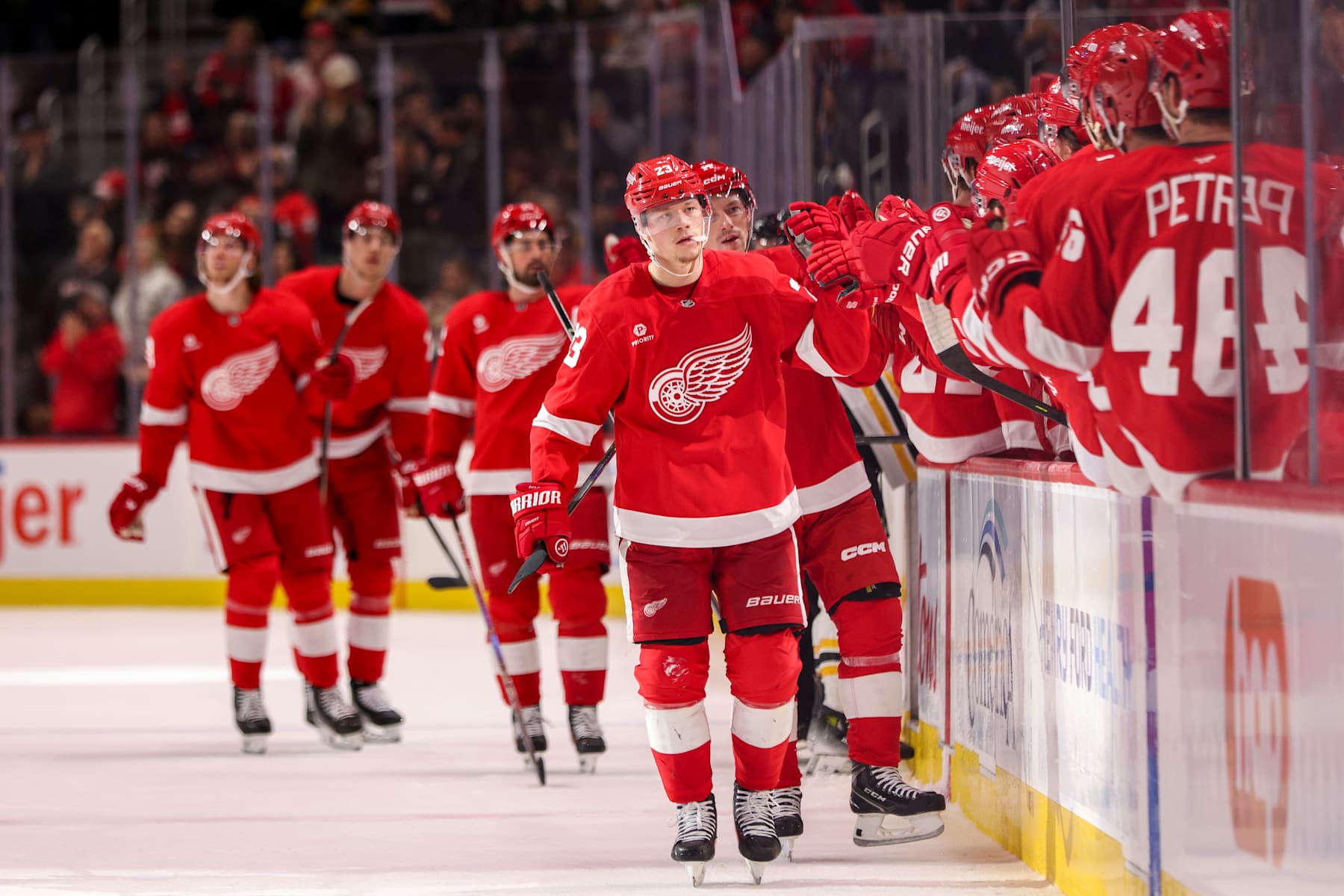 DETROIT, MICHIGAN - NOVEMBER 23: Lucas Raymond #23 of the Detroit Red Wings high fives teammates as he skates by the bench after scoring a goal to tie the game at 1-1 during the first period of a game against the Boston Bruins at Little Caesars Arena on November 23, 2024 in Detroit, Michigan. (Photo by Mike Mulholland/Getty Images)