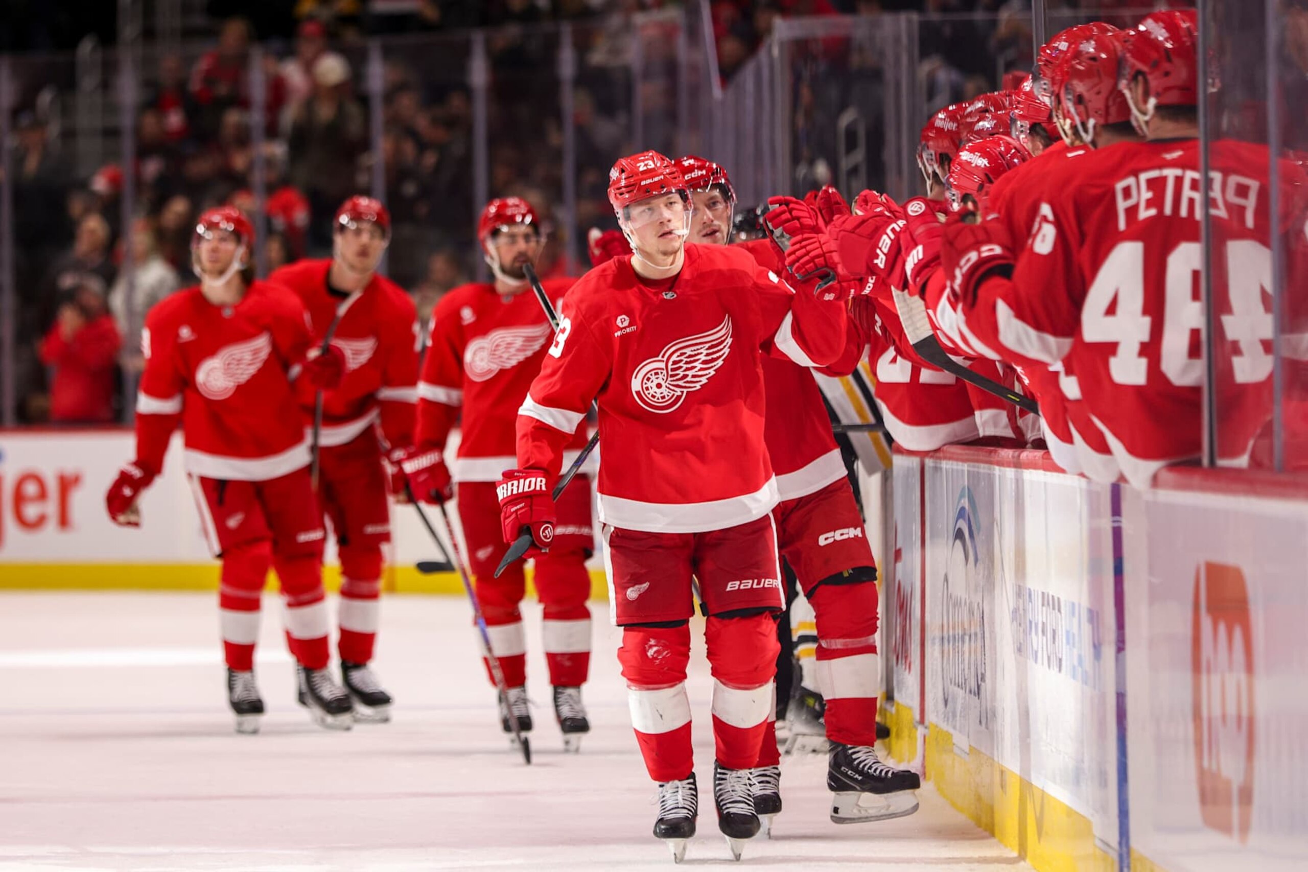 DETROIT, MICHIGAN - NOVEMBER 23: Lucas Raymond #23 of the Detroit Red Wings high fives teammates as he skates by the bench after scoring a goal to tie the game at 1-1 during the first period of a game against the Boston Bruins at Little Caesars Arena on November 23, 2024 in Detroit, Michigan. (Photo by Mike Mulholland/Getty Images)