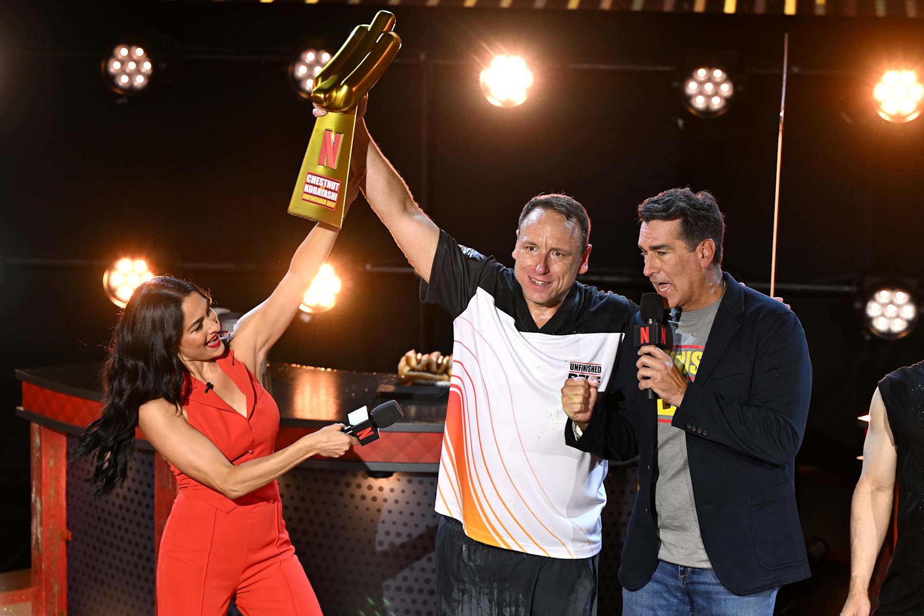 LAS VEGAS, NEVADA - SEPTEMBER 02: (L-R) Nikki Garcia, Joey Chestnut and Rob Riggle speak onstage during LIVE Chestnut vs. Kobayashi: Unfinished Beef at the Hyper X Arena at the Luxor on September 02, 2024 in Las Vegas, Nevada. (Photo by David Becker/Getty Images for Netflix © 2024)