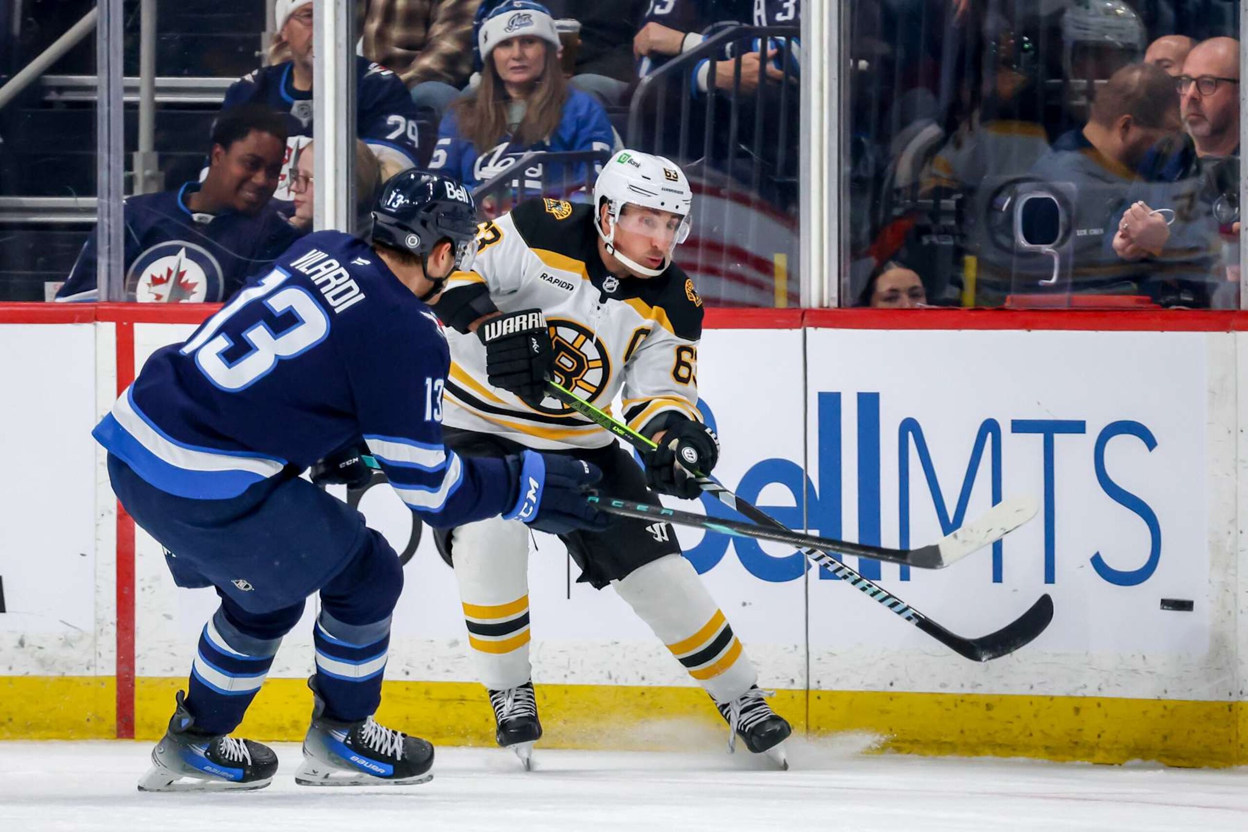 WINNIPEG, CANADA - DECEMBER 10: Brad Marchand #63 of the Boston Bruins chips the puck past Gabriel Vilardi #13 of the Winnipeg Jets during first period action at the Canada Life Centre on December 10, 2024 in Winnipeg, Manitoba, Canada. (Photo by Jonathan Kozub/NHLI via Getty Images) WINNIPEG, CANADA - DECEMBER 10: Brad Marchand #63 of the Boston Bruins chips the puck past Gabriel Vilardi #13 of the Winnipeg Jets during first period action at the Canada Life Centre on December 10, 2024 in Winnipeg, Manitoba, Canada. (Photo by Jonathan Kozub/NHLI via Getty Images)
