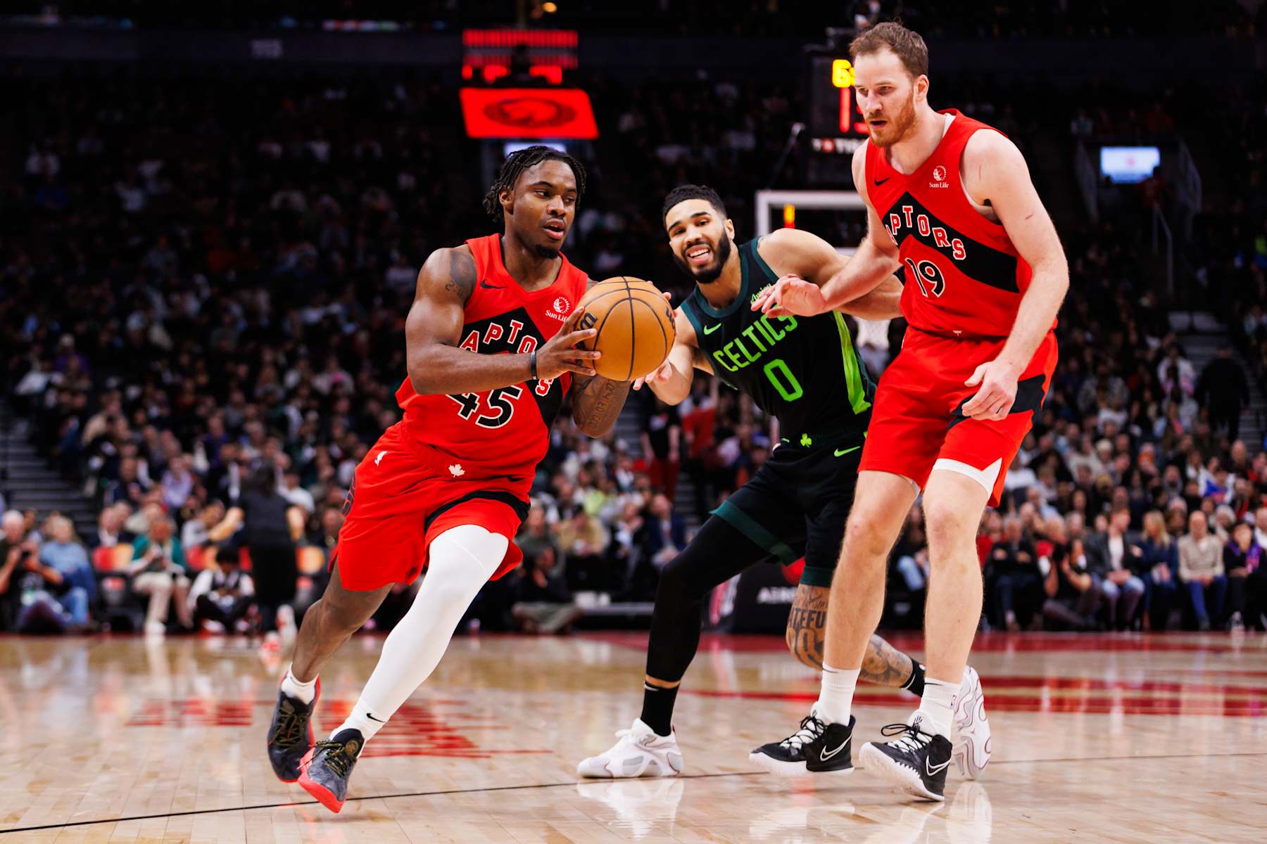 TORONTO, CANADA - JANUARY 15: Davion Mitchell #45 of the Toronto Raptors drives to the net as Jakob Poeltl #19 sets a screen on Jayson Tatum #0 of the Boston Celtics during second half of their NBA game at Scotiabank Arena on January 15, 2025 in Toronto, Canada. NOTE TO USER: User expressly acknowledges and agrees that, by downloading and or using this photograph, User is consenting to the terms and conditions of the Getty Images License Agreement. (Photo by Cole Burston/Getty Images)