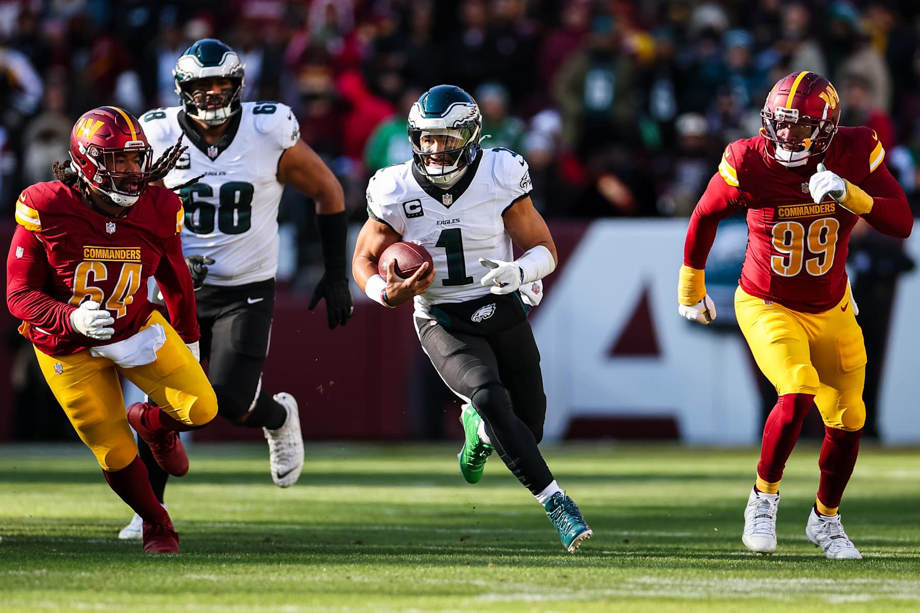 LANDOVER, MD - DECEMBER 22: Jalen Hurts #1 of the Philadelphia Eagles carries the ball as Sheldon Day #64 and Clelin Ferrell #99 of the Washington Commanders during the first half of the game at Northwest Stadium on December 22, 2024 in Landover, Maryland. (Photo by Scott Taetsch/Getty Images)