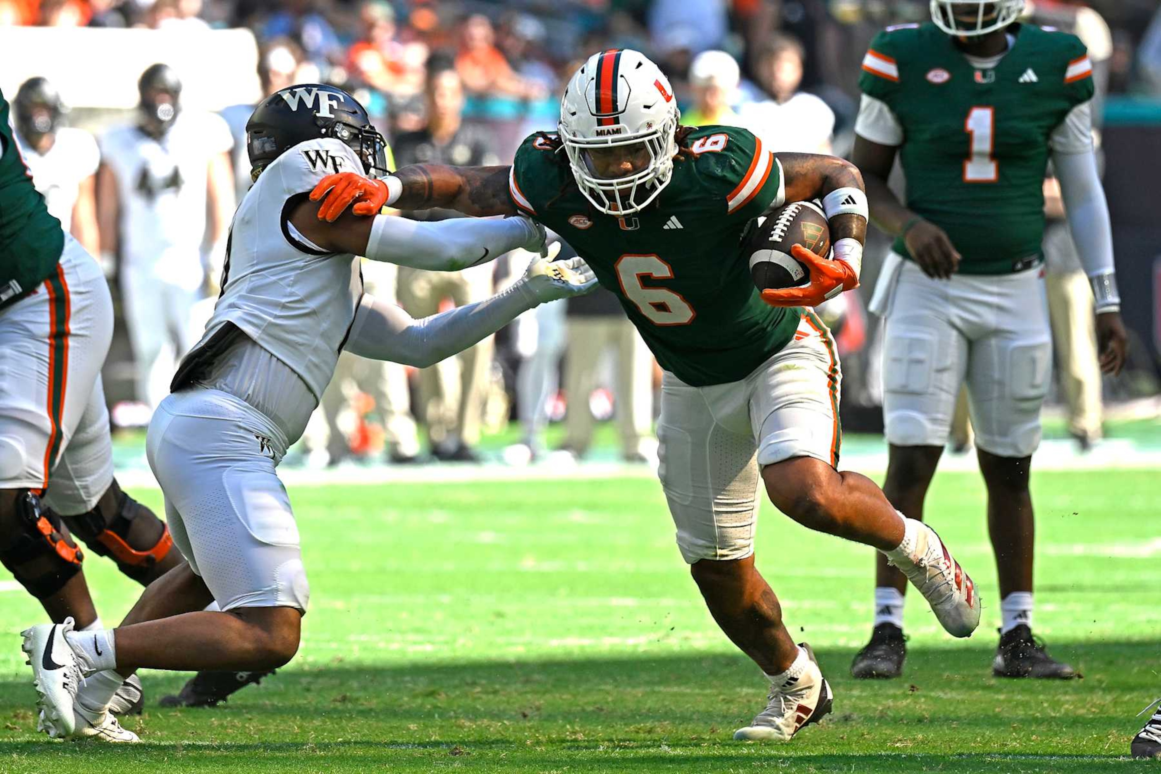 MIAMI GARDENS, FL - NOVEMBER 23: Miami running back Damien Martinez (6) holds off Wake Forest defensive back Evan Slocum (7) while carrying the ball in the first quarter as the Miami Hurricanes faced the Wake Forest Demon Deacons on November 23, 2024, at Hard Rock Stadium in Miami Gardens, Florida. (Photo by Samuel Lewis/Icon Sportswire via Getty Images) MIAMI GARDENS, FL - NOVEMBER 23: Miami running back Damien Martinez (6) holds off Wake Forest defensive back Evan Slocum (7) while carrying the ball in the first quarter as the Miami Hurricanes faced the Wake Forest Demon Deacons on November 23, 2024, at Hard Rock Stadium in Miami Gardens, Florida. (Photo by Samuel Lewis/Icon Sportswire via Getty Images)