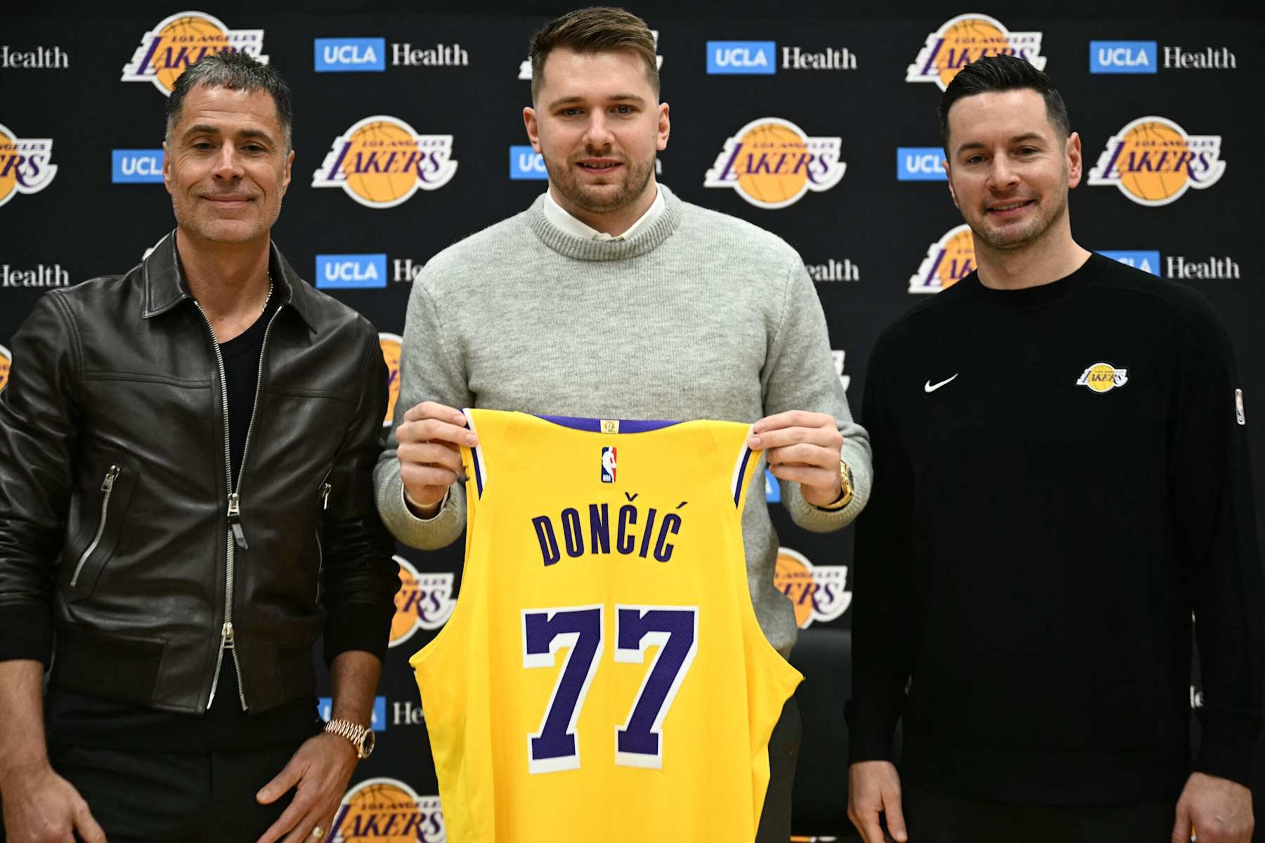 Slovenian basketball player Luka Doncic (C) holds up a jersey as he stands alongside Los Angeles Lakers head coach JJ Redick (R) and Los Angeles Lakers general manager Rob Pelinka  during a press conference introducing Doncic as the newest member of the Los Angeles Lakers, at the UCLA Health Training Center, in El Segundo, California on February 4, 2025. Slovenian star Luka Doncic said February 2, 2025 he thought he'd spend his entire NBA career in Dallas, thanking fans in Texas for making it feel like home a day after the Mavericks abruptly traded him to the Los Angeles Lakers. (Photo by Patrick T. Fallon / AFP) (Photo by PATRICK T. FALLON/AFP via Getty Images)          