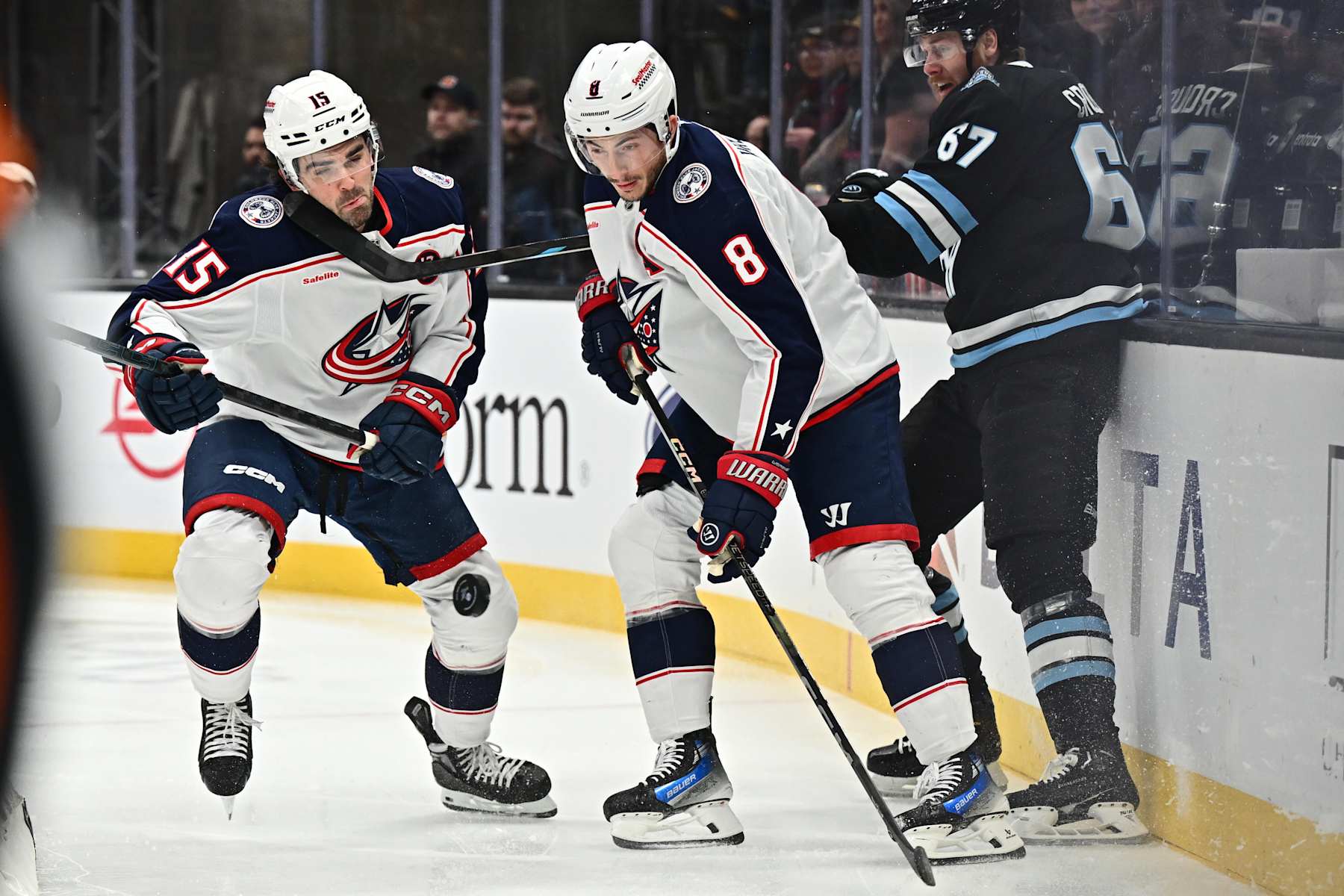 SALT LAKE CITY, UTAH - JANUARY 31:  Dante Fabbro #15 of the Columbus Blue Jackets takes a stick to the face from Lawson Crouse #67 of the Utah Hockey Club while battling for a puck with Zach Werenski #8 of the Columbus Blue Jackets in the first period on January 31, 2025 at Delta Center in Salt Lake City, Utah. (Photo by Jamie Sabau/NHLI via Getty Images)