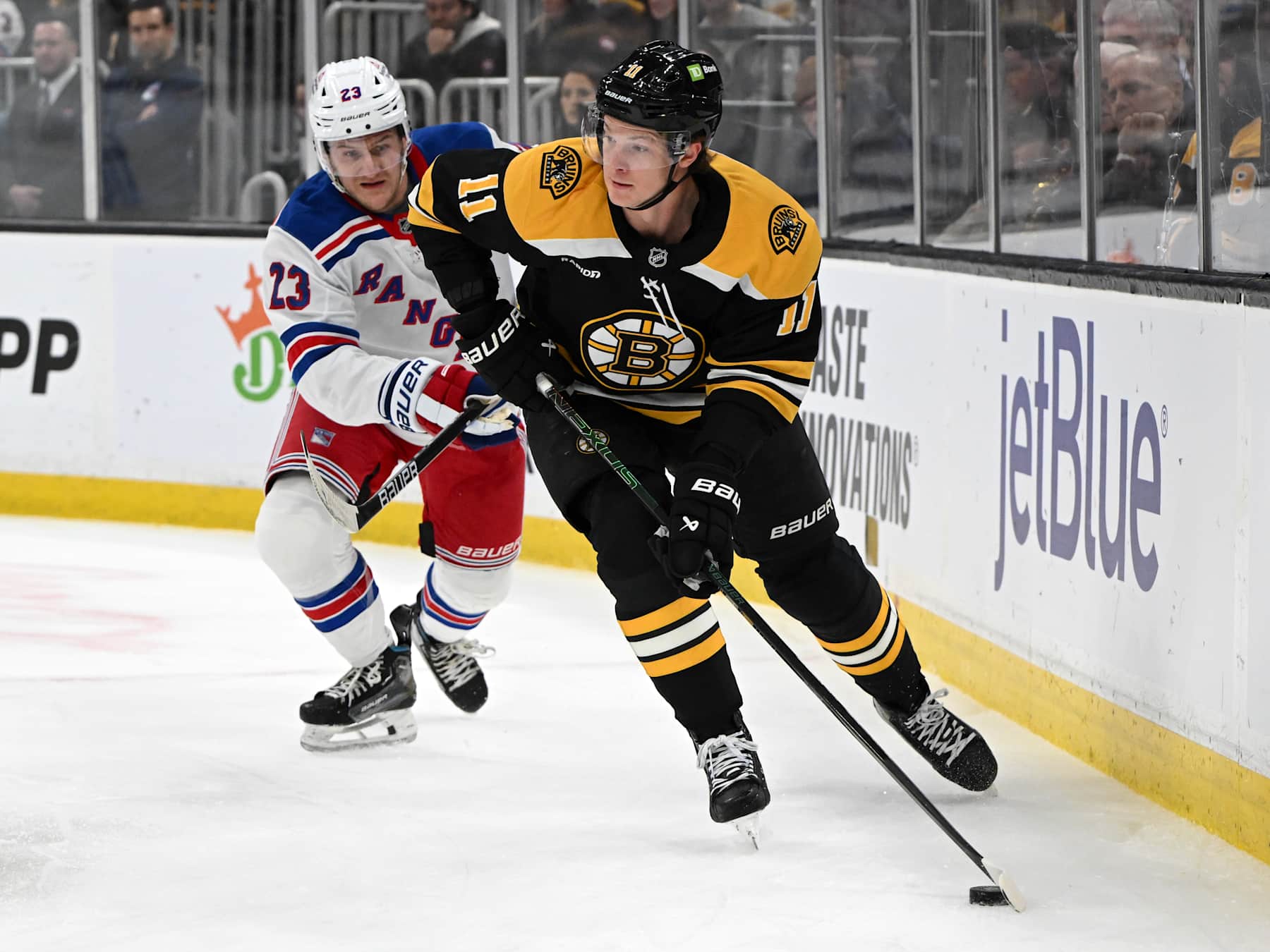 BOSTON, MASSACHUSETTS - FEBRUARY 01: Trent Frederic #11 of the Boston Bruins skates the puck away from Adam Fox #23 of the New York Rangers during the first period at the TD Garden on February 01, 2025 in Boston, Massachusetts. (Photo by Brian Fluharty/Getty Images)