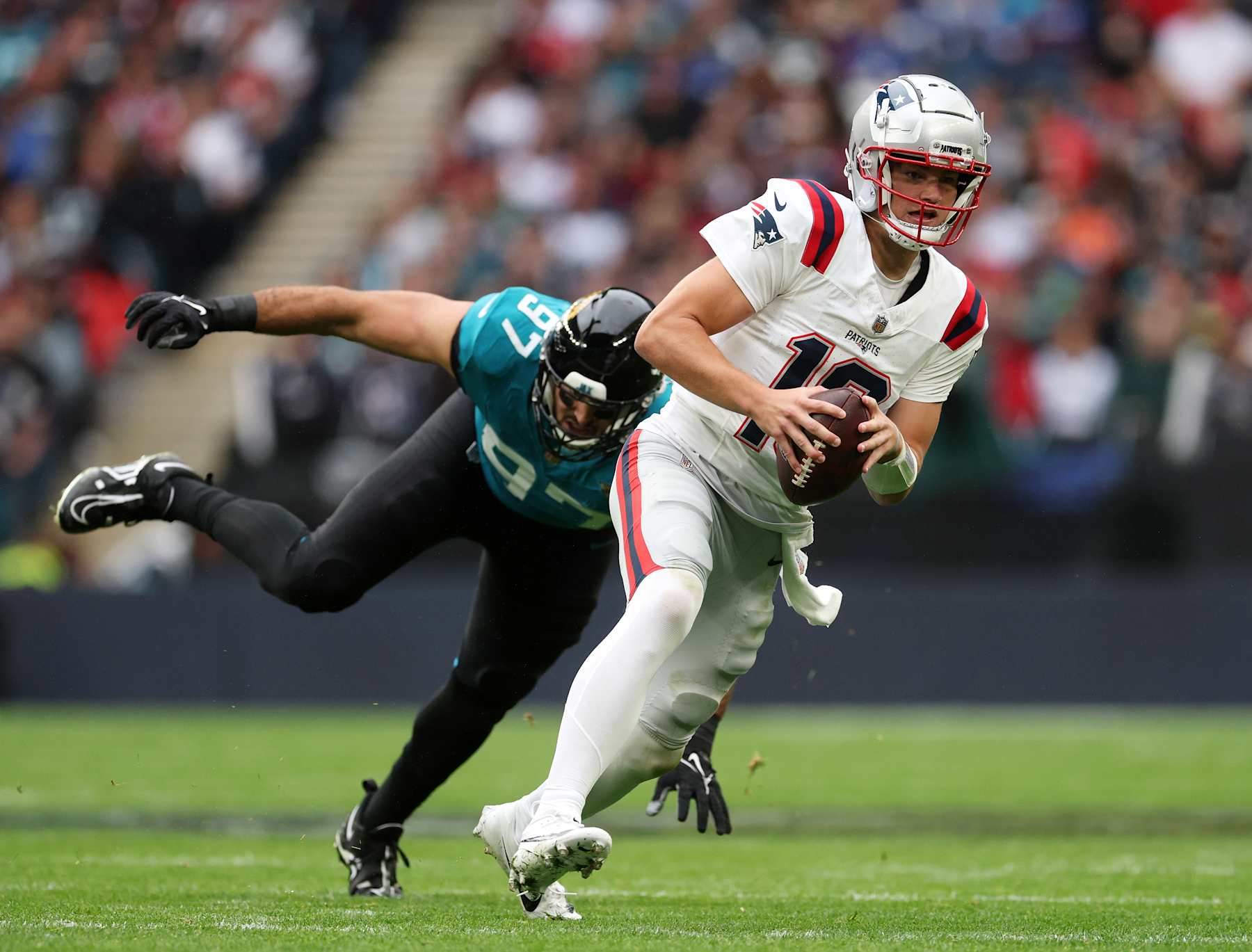 LONDON, ENGLAND - OCTOBER 20: Drake Maye of New England Patriots is challenged by Joe Gaziano of Jacksonville Jaguars during the NFL match between New England Patriots and Jacksonville Jaguars at Wembley Stadium on October 20, 2024 in London, England. (Photo by Richard Heathcote/Getty Images)