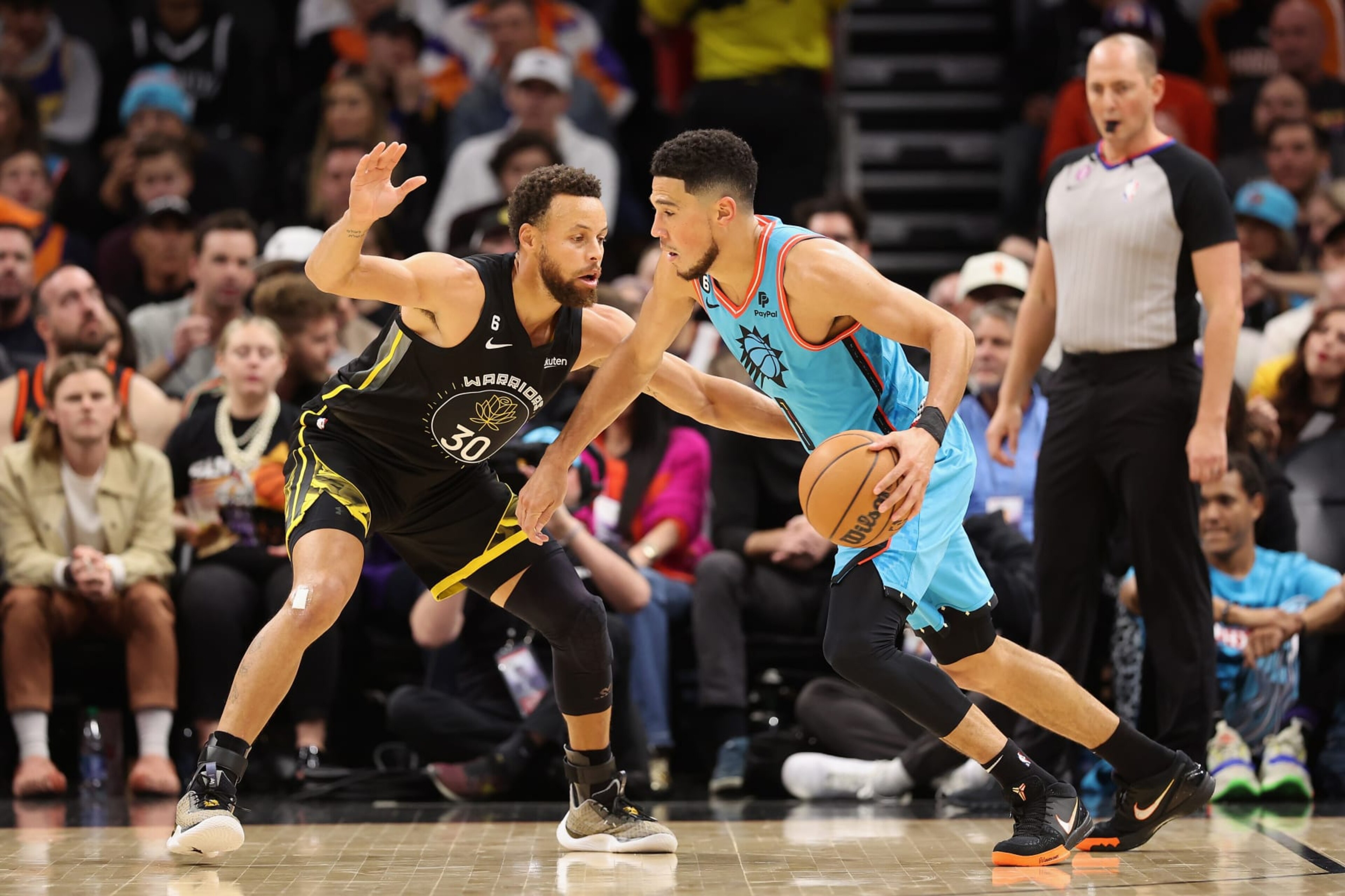 PHOENIX, ARIZONA - NOVEMBER 16:  Devin Booker #1 of the Phoenix Suns drives the ball against Stephen Curry #30 of the Golden State Warriors during the first half of the NBA game at Footprint Center on November 16, 2022 in Phoenix, Arizona. The Suns defeated the Warriors 130-119.  NOTE TO USER: User expressly acknowledges and agrees that, by downloading and or using this photograph, User is consenting to the terms and conditions of the Getty Images License Agreement.  (Photo by Christian Petersen/Getty Images)