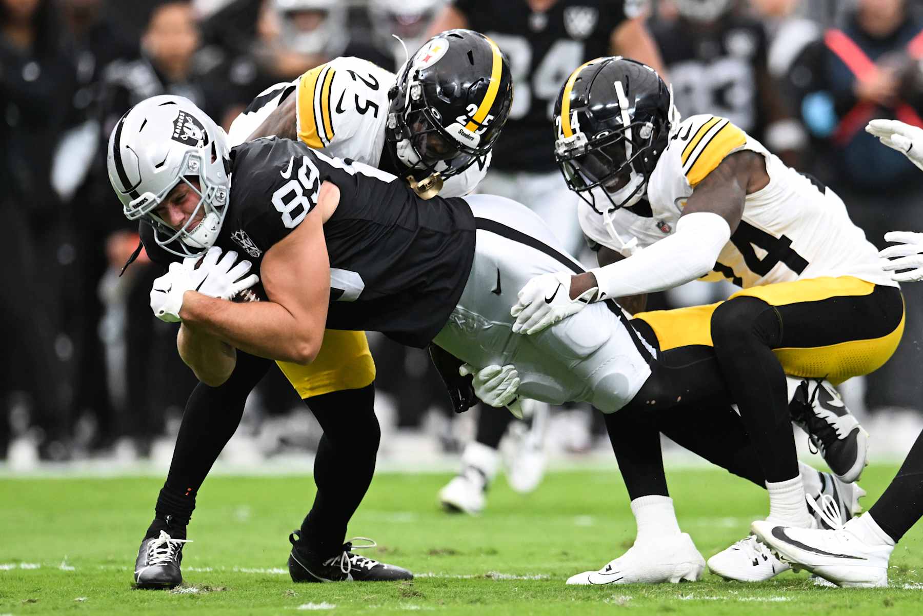 LAS VEGAS, NEVADA - OCTOBER 13: Brock Bowers #89 of the Las Vegas Raiders	dives as he is tackled by DeShon Elliott #25 and Joey Porter Jr. #24 of the Pittsburgh Steelers in the first quarter of a game at Allegiant Stadium on October 13, 2024 in Las Vegas, Nevada. (Photo by Candice Ward/Getty Images)