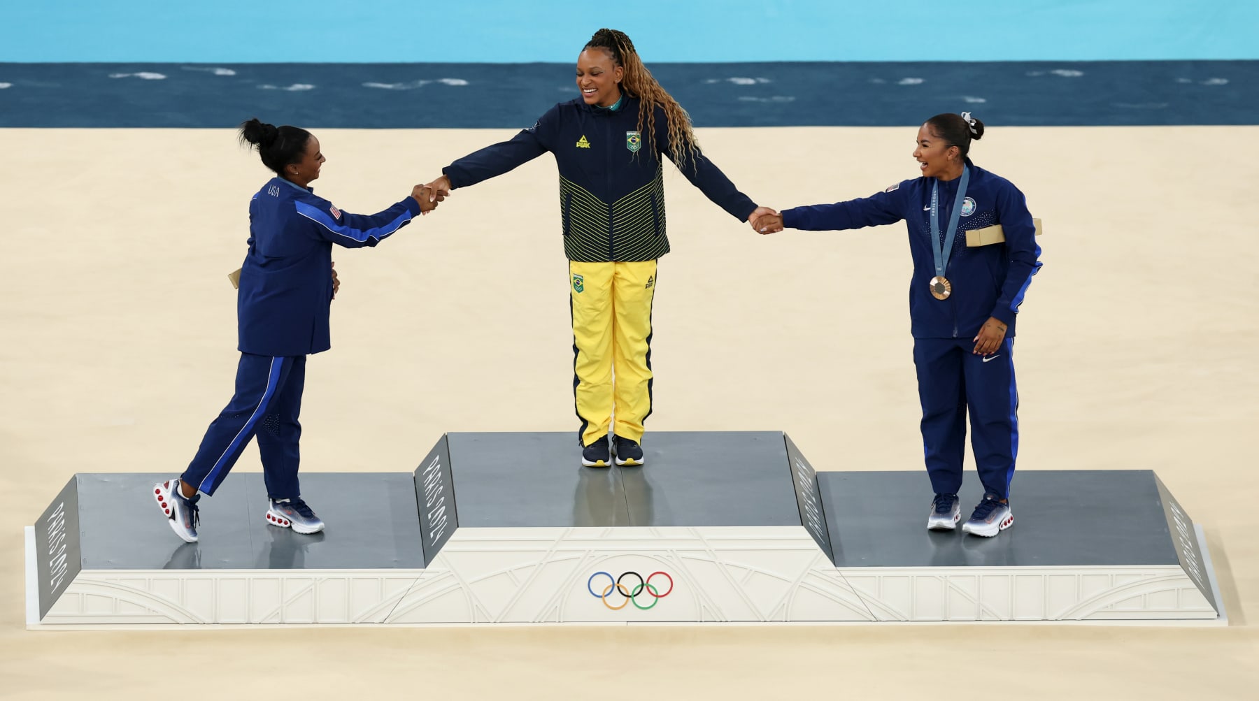 PARIS, FRANCE - AUGUST 05: Gold medalist Rebeca Andrade (C) of Team Brazil, silver medalist Simone Biles (L) of Team United States and bronze medalist Jordan Chiles (R) of Team United States celebrate on the podium at the Artistic Gymnastics Women's Floor Exercise Medal Ceremony on day ten of the Olympic Games Paris 2024 at Bercy Arena on August 05, 2024 in Paris, France. (Photo by Elsa/Getty Images)