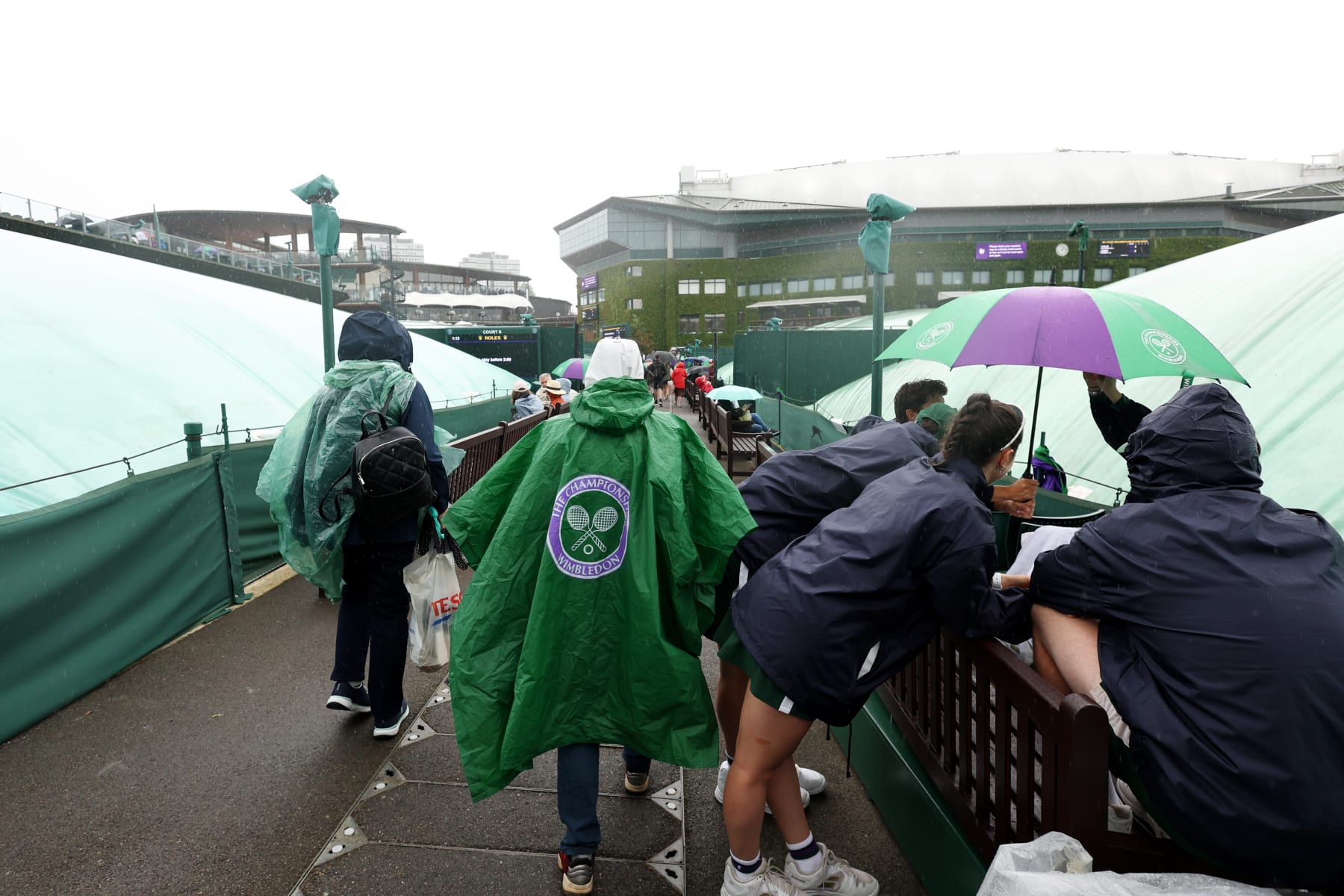 LONDON, ENGLAND - JULY 04: Spectators shelter from the rain with umbrellas as play is suspended during day two of The Championships Wimbledon 2023 at All England Lawn Tennis and Croquet Club on July 04, 2023 in London, England. (Photo by Julian Finney/Getty Images)