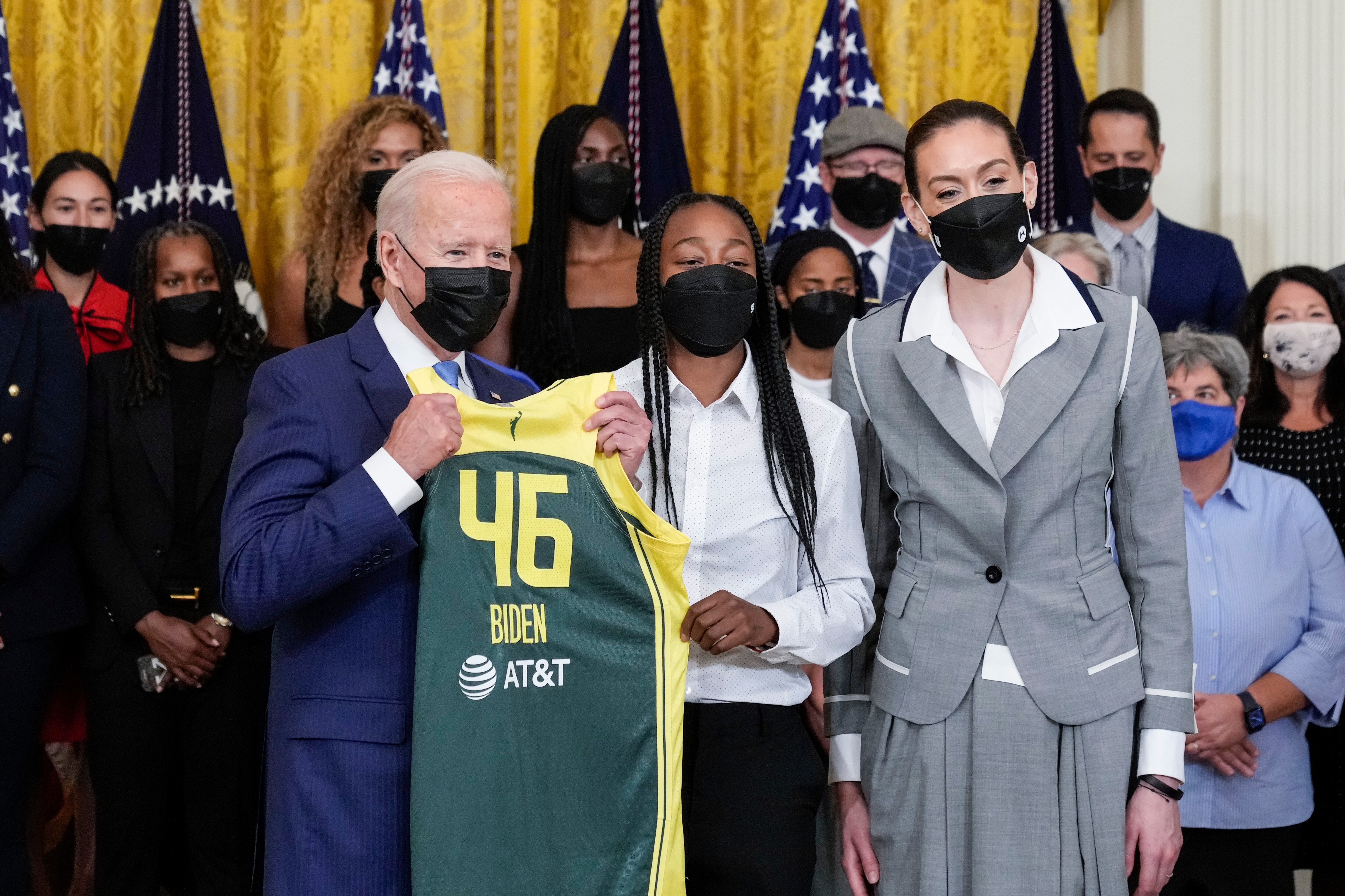 WASHINGTON, DC - AUGUST 23: (L-R) U.S. President Joe Biden accepts a jersey from Jewell Lloyd and  Breanna Stewart during an event with the 2020 WNBA champions Seattle Storm in the East Room of the White House on August 23, 2021 in Washington, DC. The Storm defeated the Last Vegas Aces in the 2020 WNBA Finals to win their 4th title as a franchise. (Photo by Drew Angerer/Getty Images)