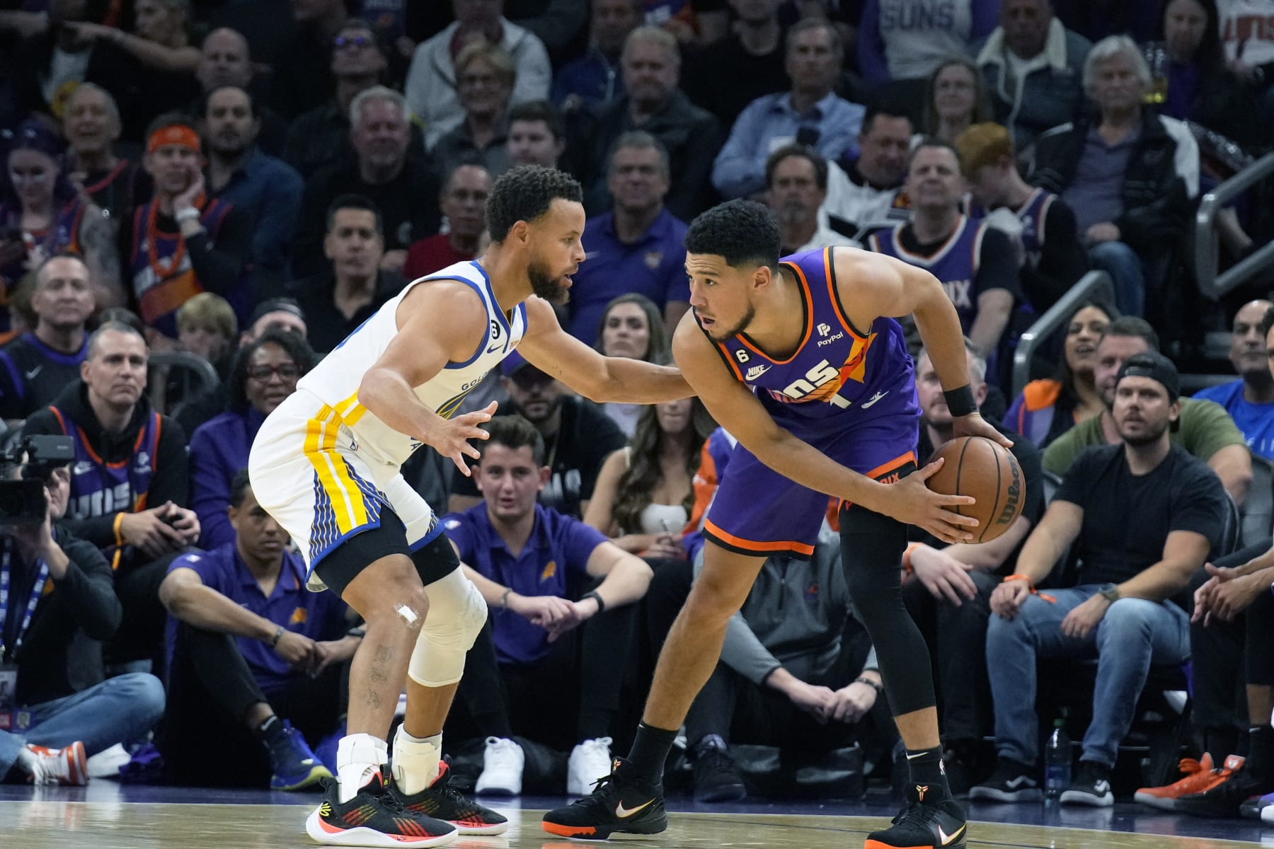 Golden State Warriors guard Stephen Curry and Phoenix Suns guard Devin Booker (1) face off during the first half of an NBA basketball game, Tuesday, Oct. 25, 2022, in Phoenix. (AP Photo/Rick Scuteri)