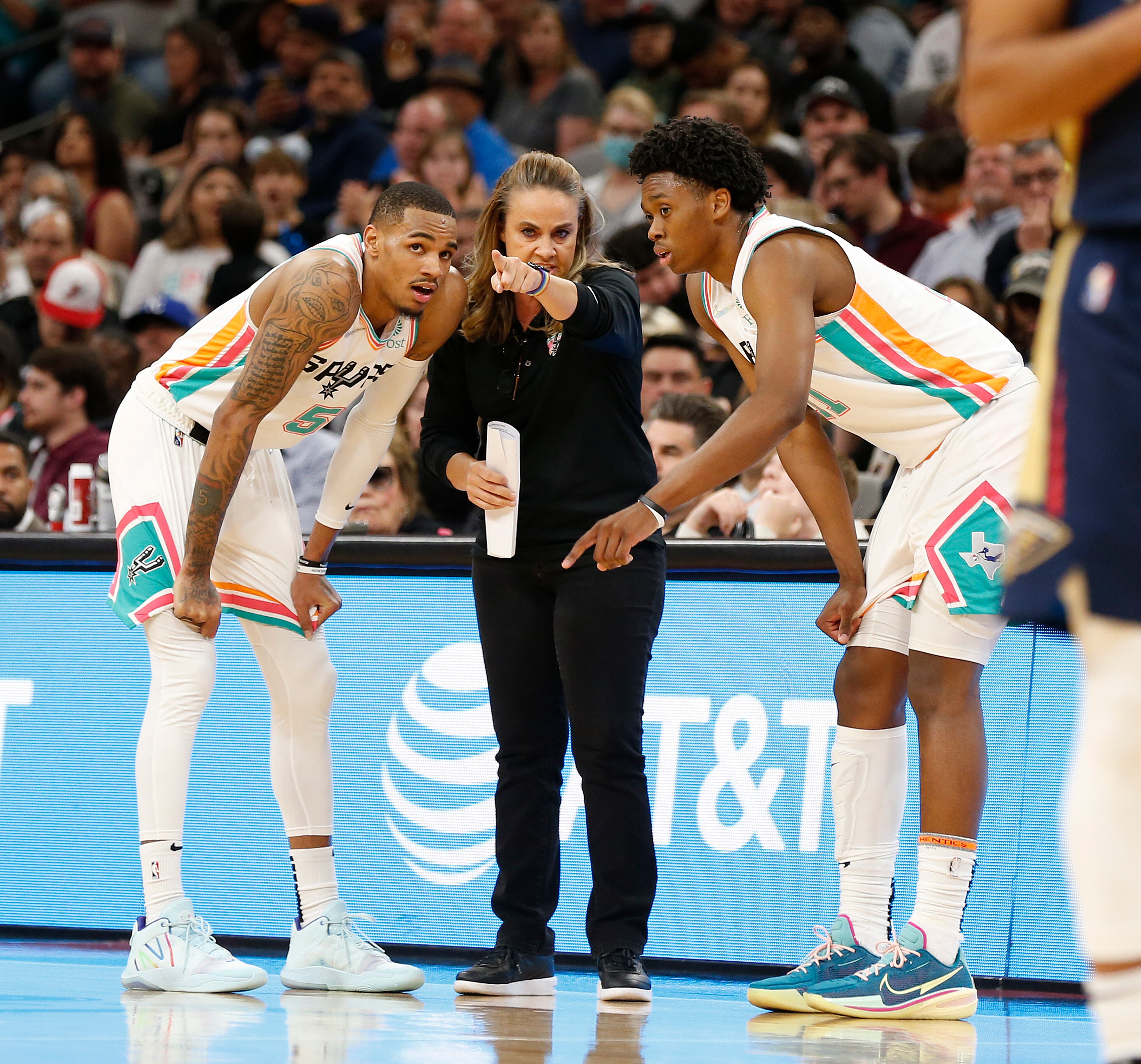 SAN ANTONIO, TX - MARCH 18: Dejounte Murray #5 and Josh Primo #11 of the San Antonio Spurs listen to assistant coach Becky Hammond in the first half at AT&T Center on March 18,  2022 in San Antonio, Texas. NOTE TO USER: User expressly acknowledges and agrees that, by downloading and or using this photograph, User is consenting to terms and conditions of the Getty Images License Agreement. (Photo by Ronald Cortes/Getty Images)