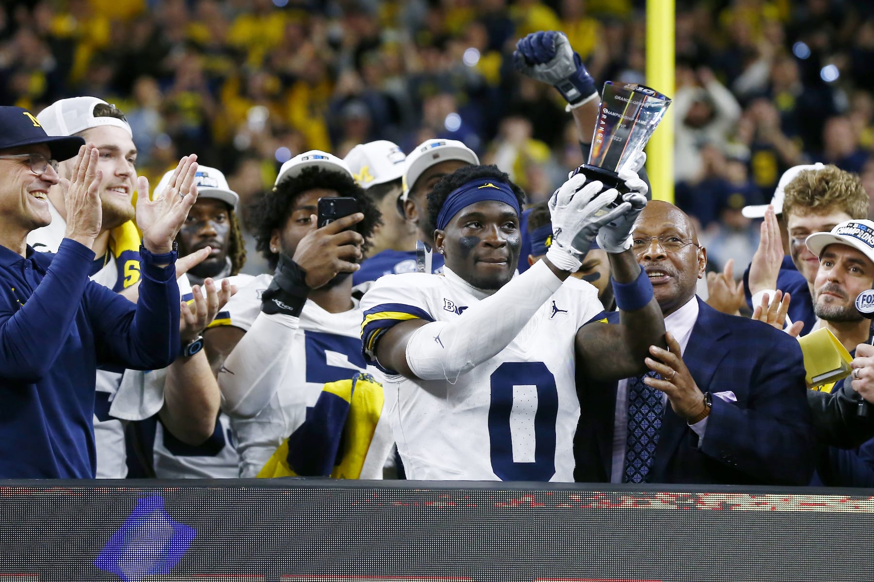 INDIANAPOLIS, IN - DECEMBER 02: Michigan Wolverines defensive back Mike Sainristil (0) raises the B1G Most Valuable Player trophy during the Big Ten Championship Game between the Michigan Wolverines and the Iowa Hawkeyes on December 02, 2023 at Lucas Oil Stadium in Indianapolis,IN.  (Photo by Jeffrey Brown/Icon Sportswire via Getty Images)