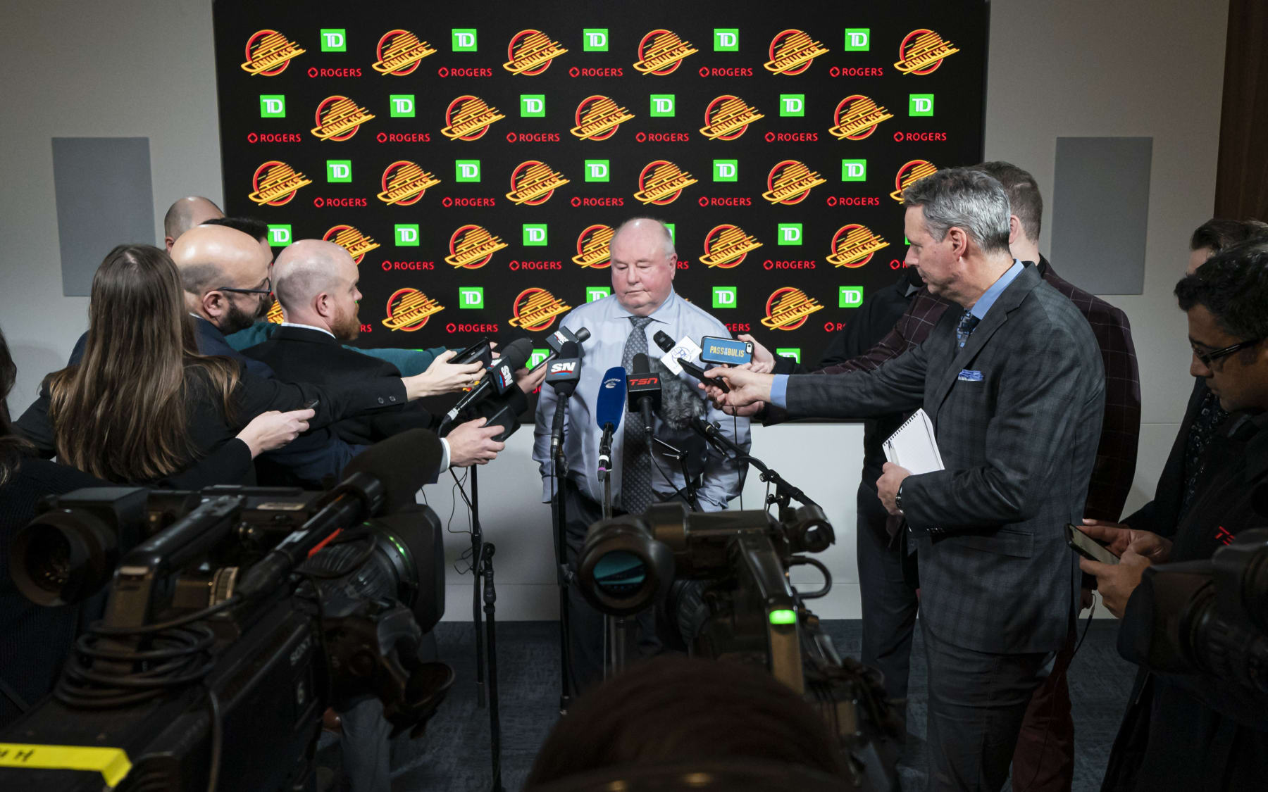 VANCOUVER, CANADA - JANUARY 21:  Reporters surround Bruce Boudreau head coach of the Vancouver Canucks during his last post-game press conference after the Canucks lost to the Edmonton Oilers on January, 21, 2023 at Rogers Arena in Vancouver, British Columbia, Canada. Boudreau was fired the next day.  (Photo by Rich Lam/Getty Images)