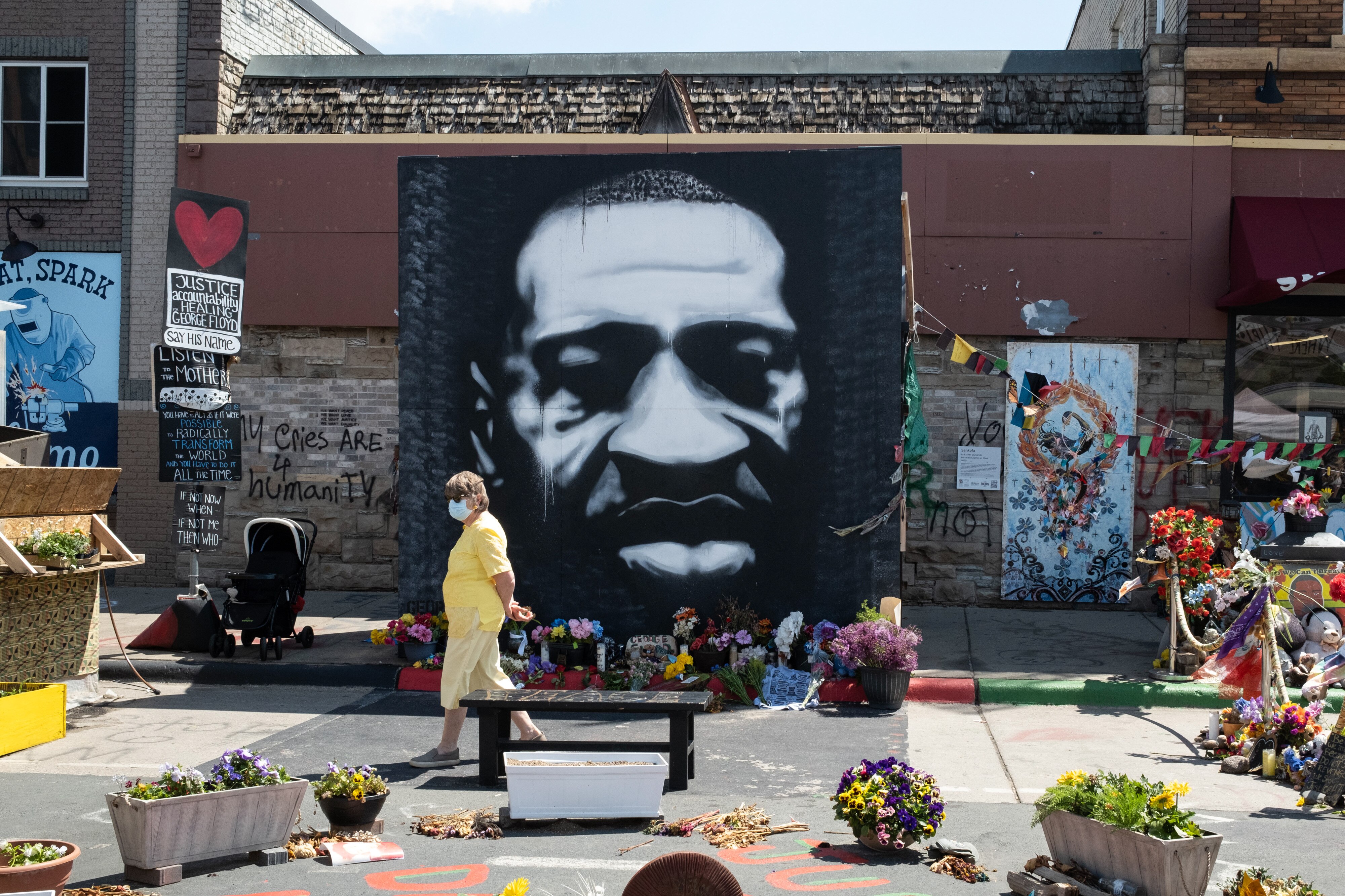 A person wearing a protective mask walks past a mural depicting George Floyd during a 'Rise and Remember' event at George Floyd Square in Minneapolis, Minnesota, U.S., on Tuesday, May 25, 2021. Since George Floyd was murdered on May 25, 2020, the city at the center of a national reckoning on race and policing has sought to reinvent itself, trying on different iterations of the change that residents say is necessary to move forward. Photographer: Tim Evans/Bloomberg via Getty Images