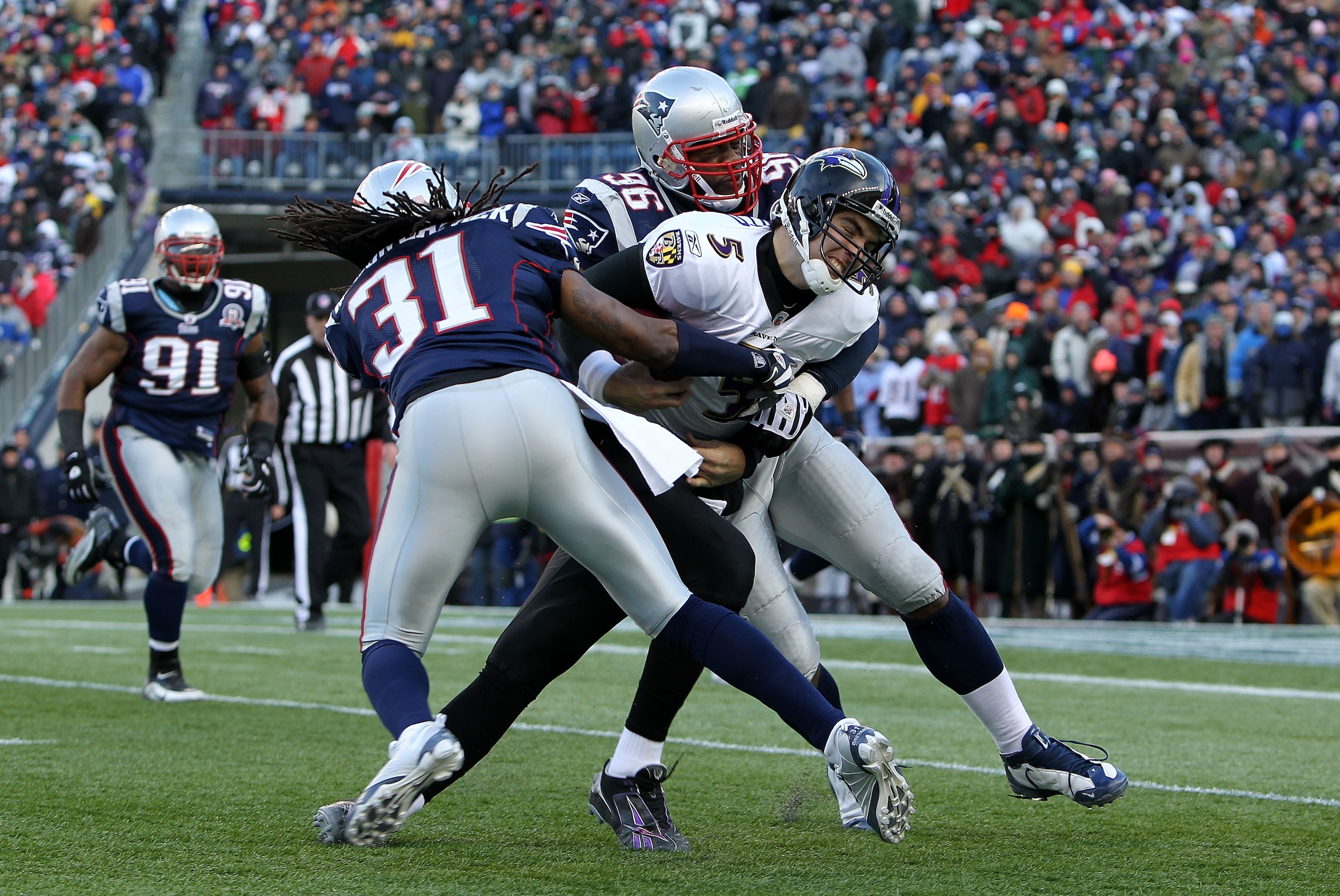 FOXBORO, MA - JANUARY 10:  Quarterback Joe Flacco #5 of the Baltimore Ravens is hit as he runs with the ball by Brandon Meriweather #31 and Adalius Thomas #96 of the New England Patriots during the 2010 AFC wild-card playoff game at Gillette Stadium on Ja