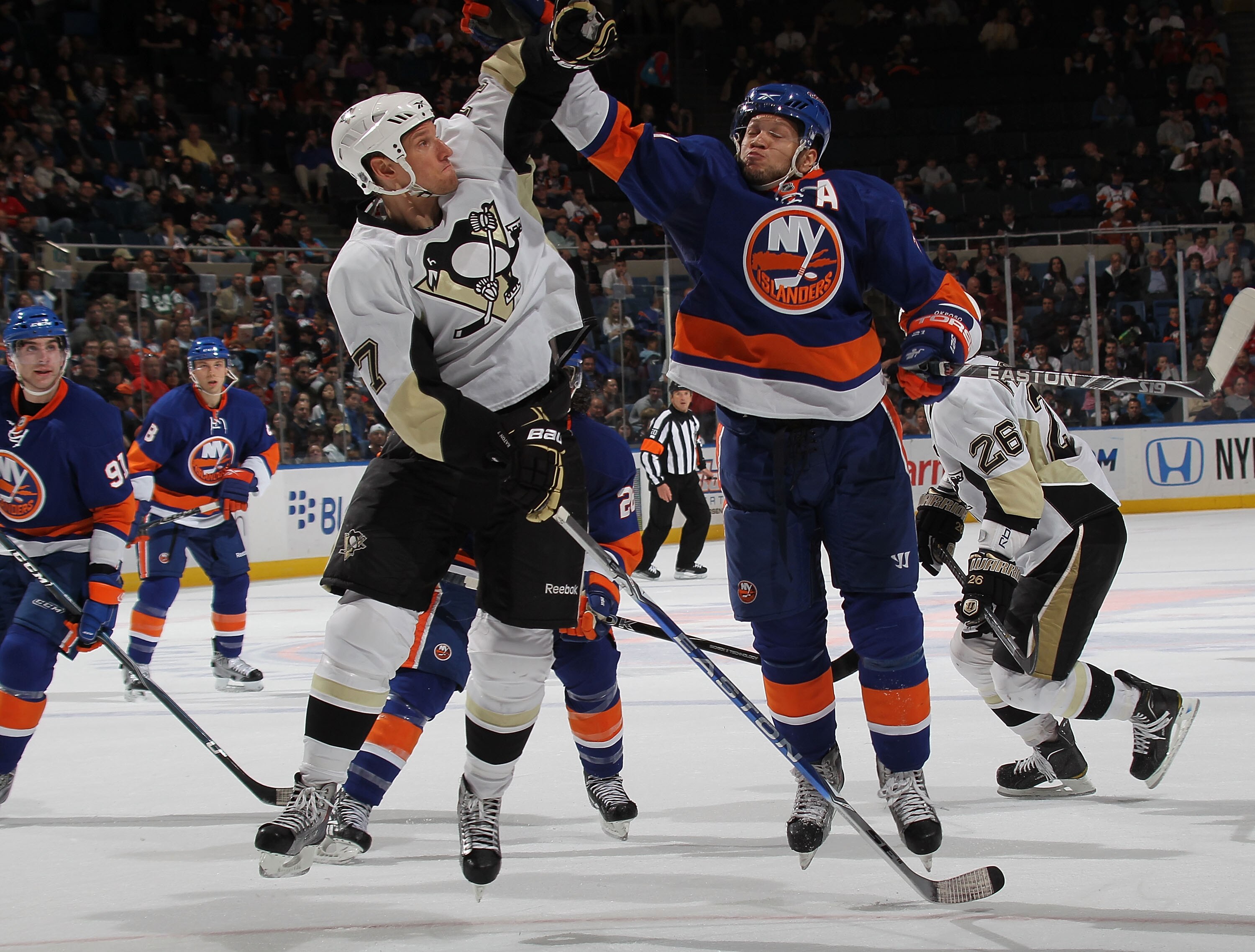 UNIONDALE, NY - APRIL 11: Kyle Okposo #21 of the New York Islanders and Mark Eaton #7 of the Pittsburgh Penguins reach for the puck at the Nassau Coliseum on April 11, 2010 in Uniondale, New York.  (Photo by Bruce Bennett/Getty Images)