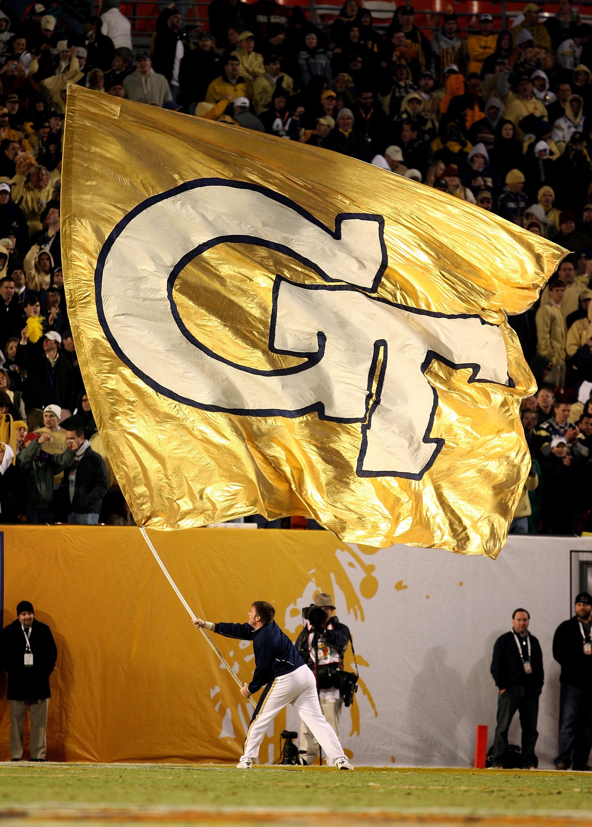 MIAMI GARDENS, FL - JANUARY 05:  A male cheerleader from the Georgia Tech Yellow Jackets waves a giant flag in support of his team against the Iowa Hawkeyes during the FedEx Orange Bowl at Land Shark Stadium on January 5, 2010 in Miami Gardens, Florida.  