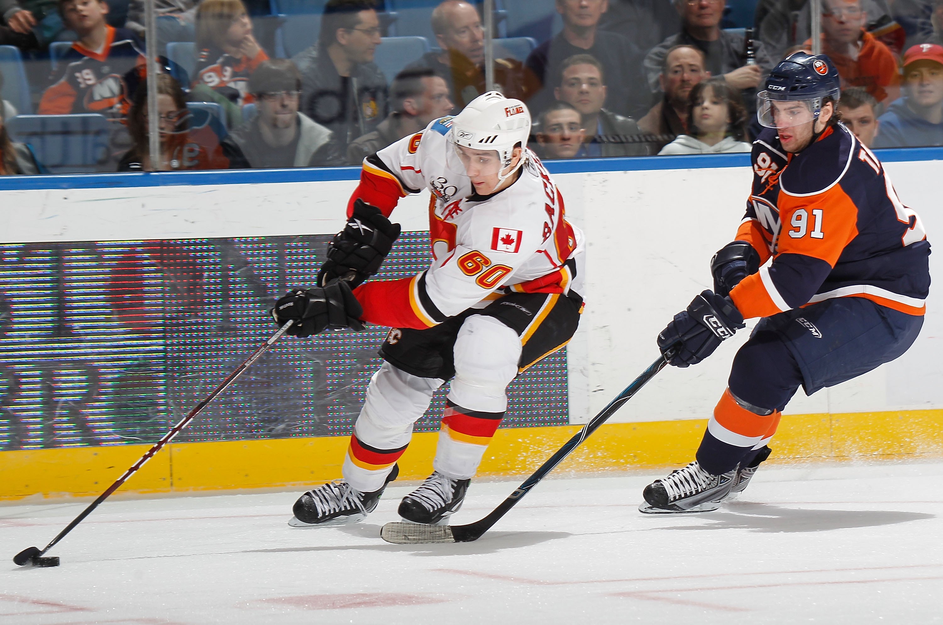 UNIONDALE, NY - MARCH 25:  Mikael Backlund #60 of the Calgary Flames skates with the puck in front of  John Tavares #91 of the New York Islanders during an NHL game at the Nassau Coliseum on March 25, 2010 in Uniondale, New York.  (Photo by Paul Bereswill
